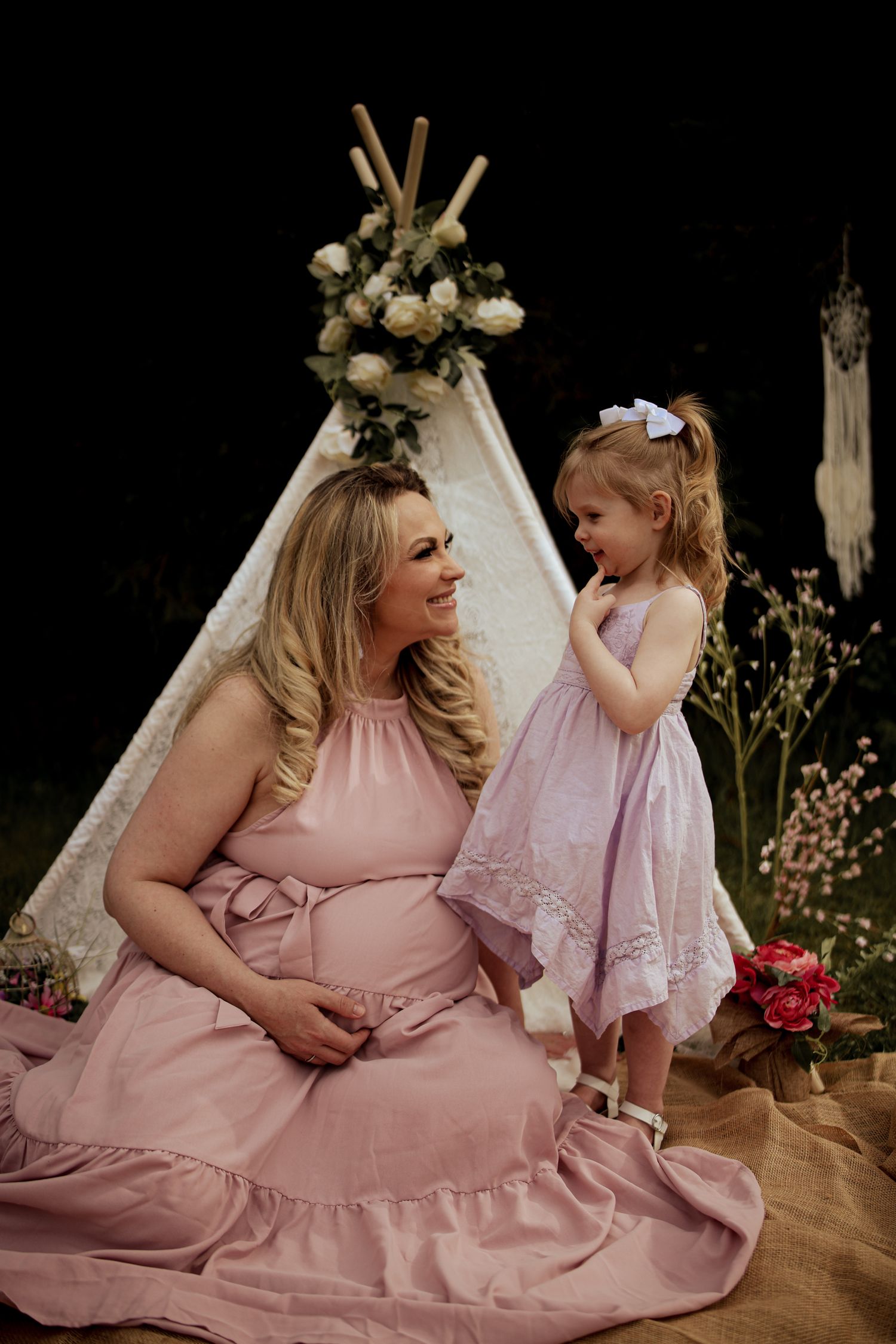 Mother and daughter in matching pink dresses share tender moments during a studio photo session.
