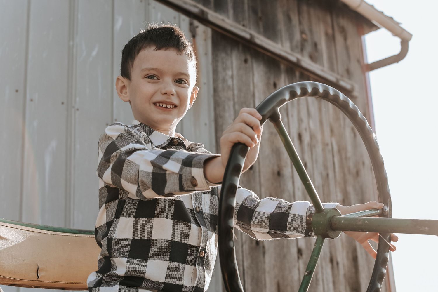 A child wearing a black and white checkered shirt plays with a vintage metal steering wheel outdoors.