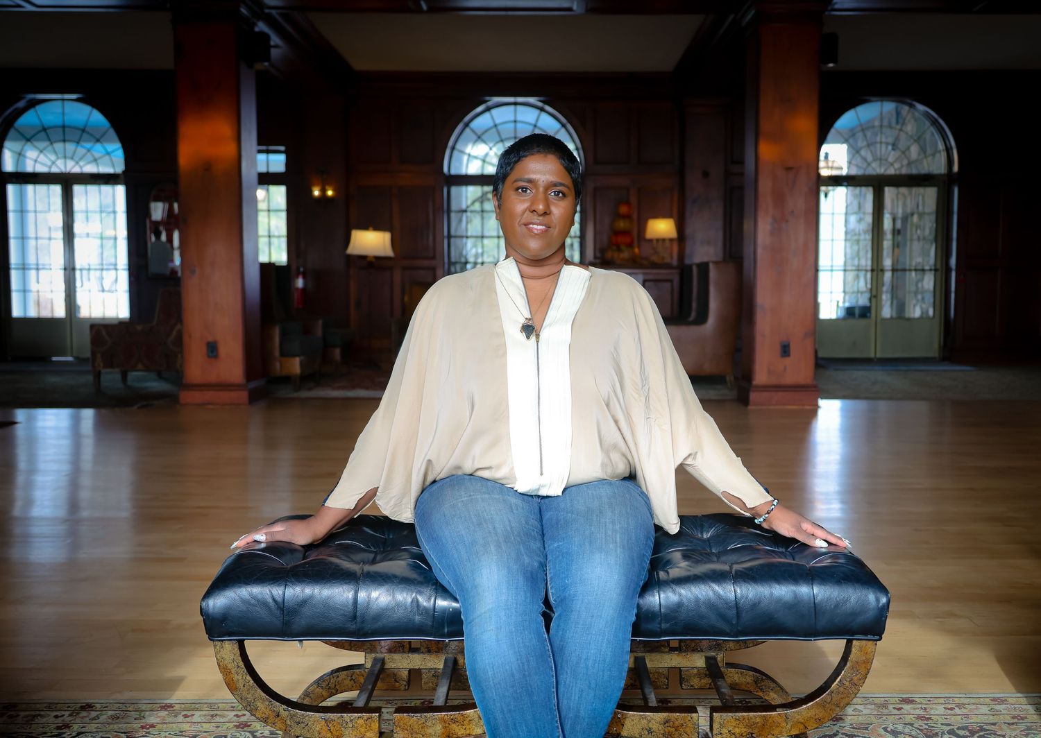 A person in jeans sits on a curved black bench in an empty indoor space with warm lighting and windows.