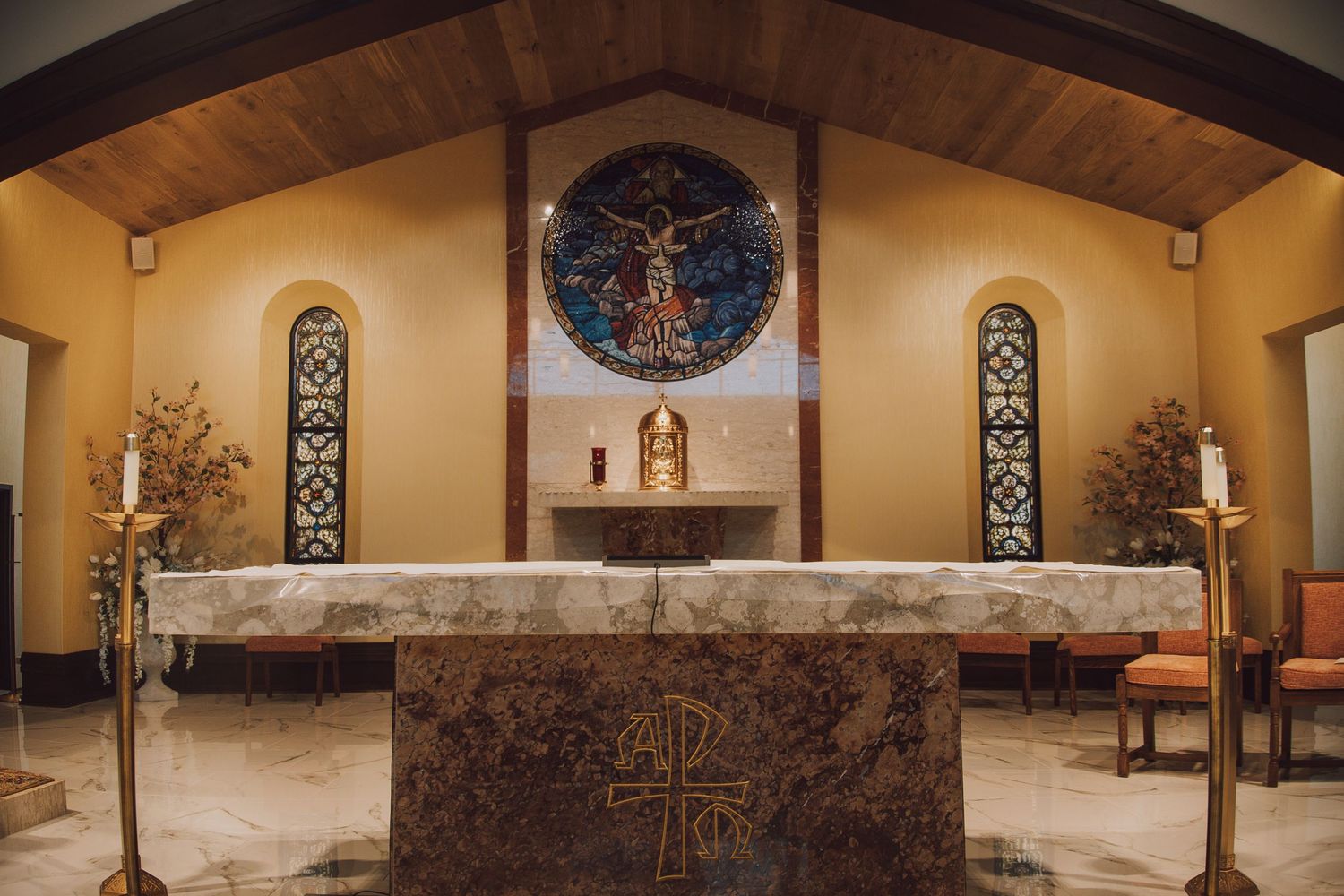 Interior panorama of a Catholic church sanctuary showing wooden beams, stained glass windows, and religious artwork.