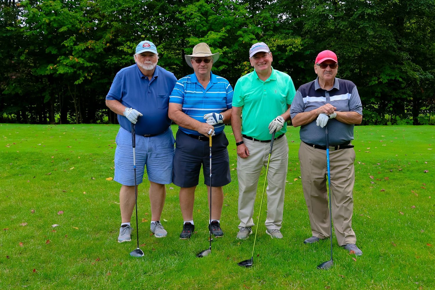 Four golfers stand together on a lush green course holding their clubs during a round of golf.