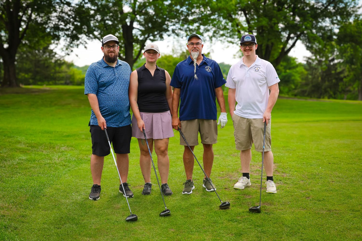Four golfers stand together with their clubs on a lush green golf course on a sunny day.