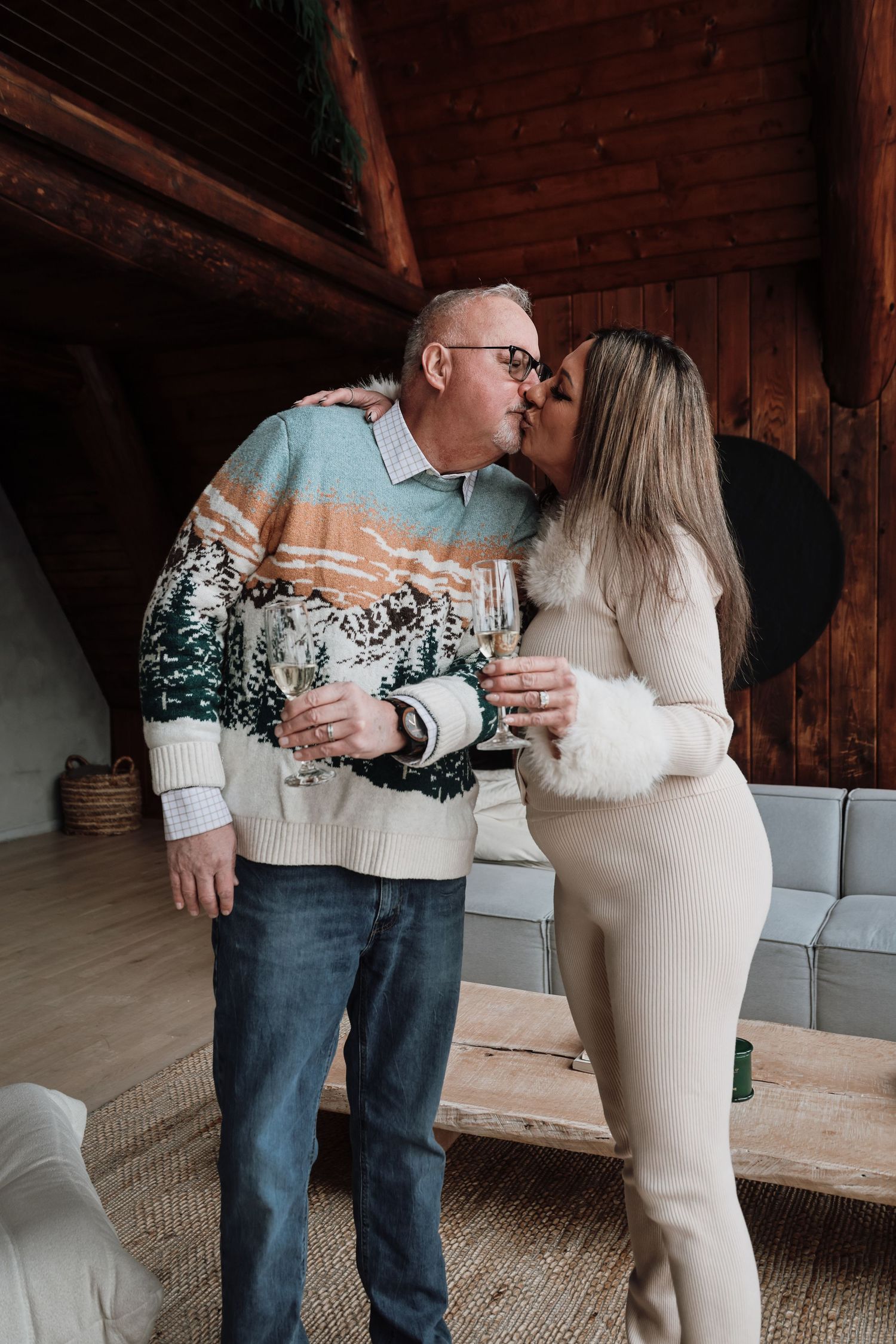 Couple in cozy winter sweaters share an intimate moment in a rustic cabin setting.