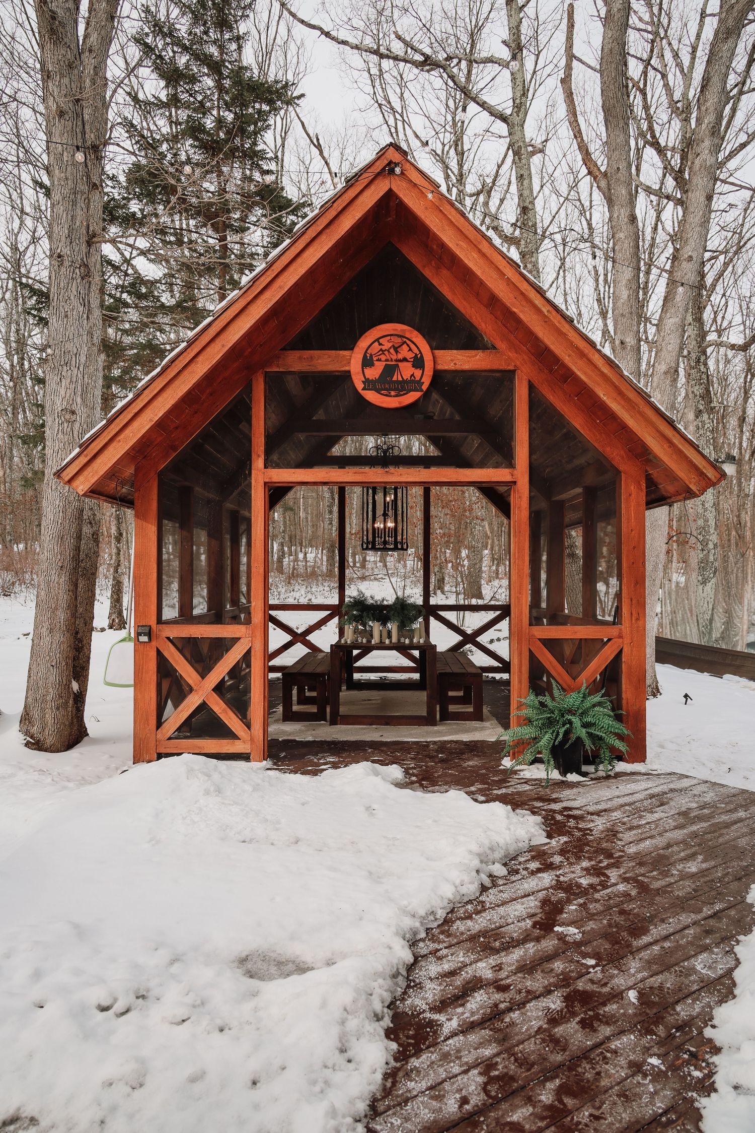 A series of wooden shelters with orange-stained roofs stand in a snowy forest setting during winter.
