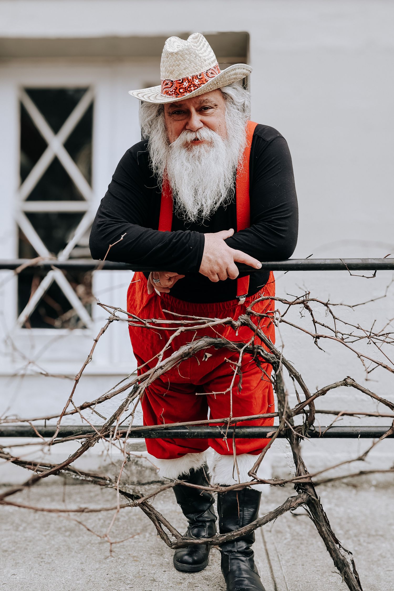 Person wearing red vest and black boots sits on bare winter tree branch against white wall.
