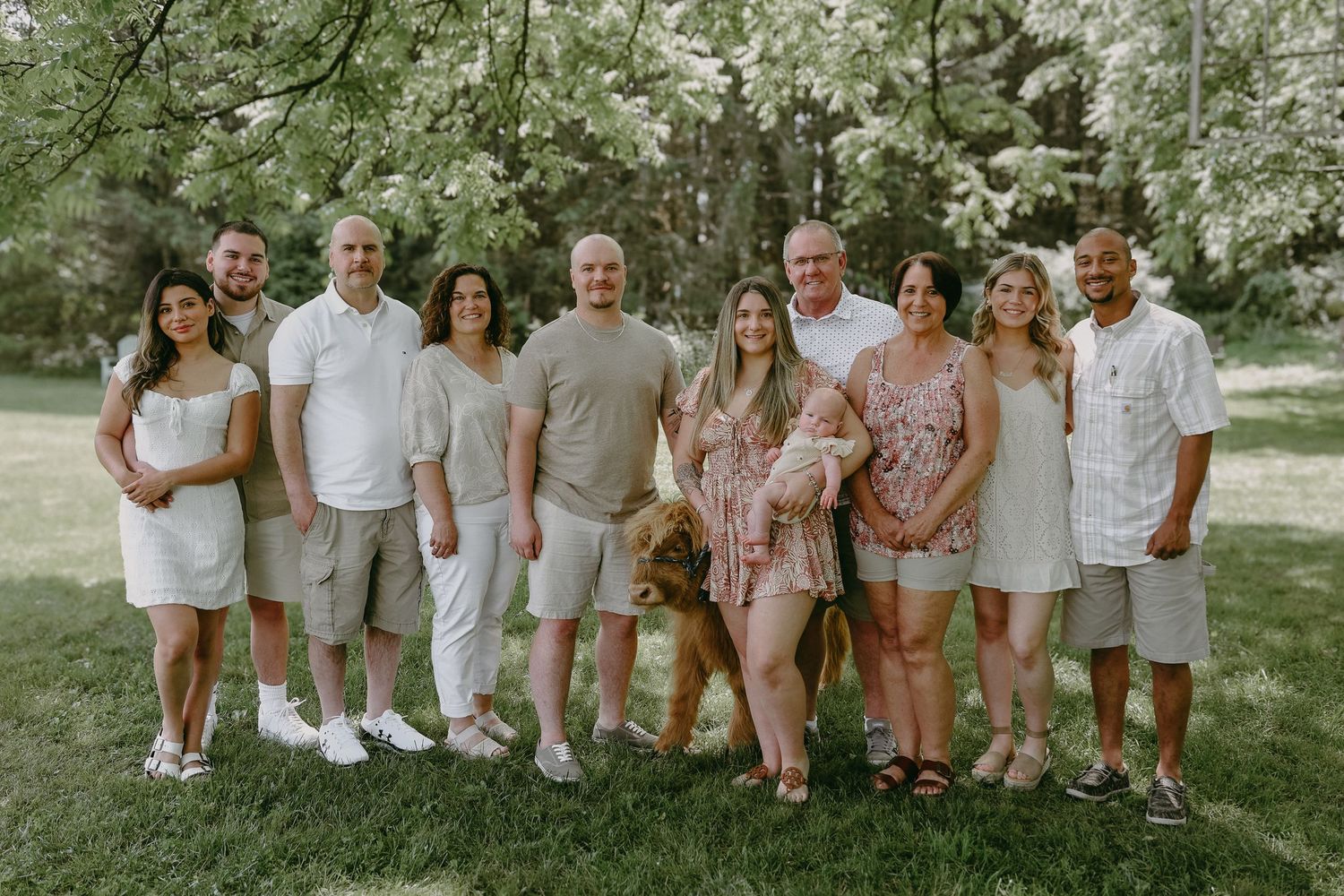 Group of people wearing coordinated white and beige outfits pose together outdoors in a garden setting.