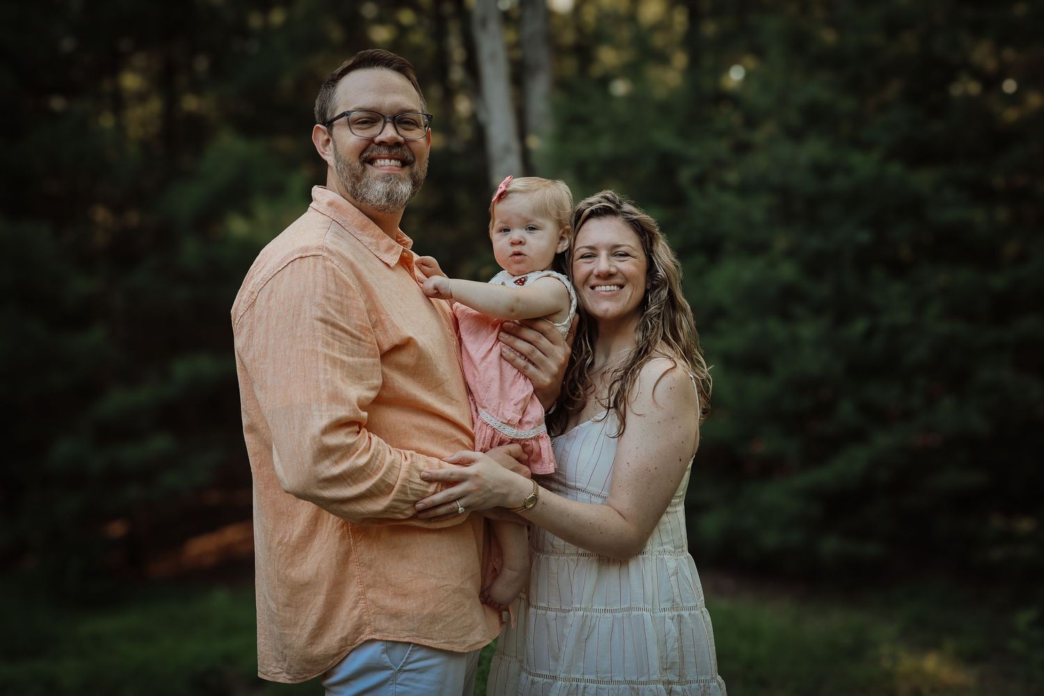 A family shares tender moments together during an outdoor photo session in a wooded setting at sunset.