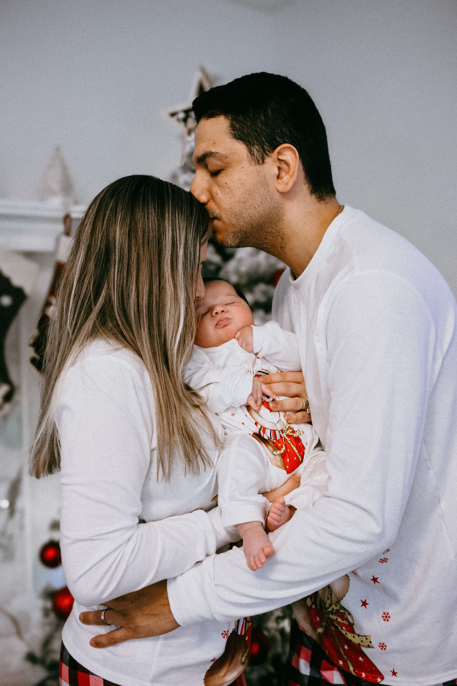 A series of intimate family photos showing parents in white shirts embracing their baby during Christmas season.