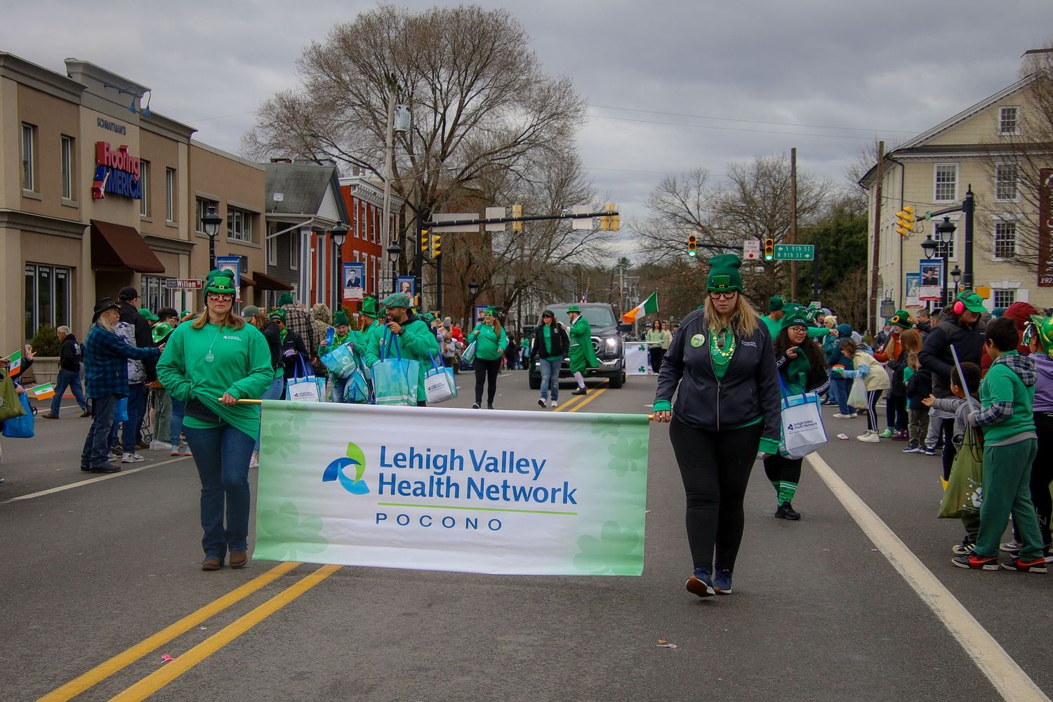 Parade participants march down a street carrying green banners and signs during a community celebration.