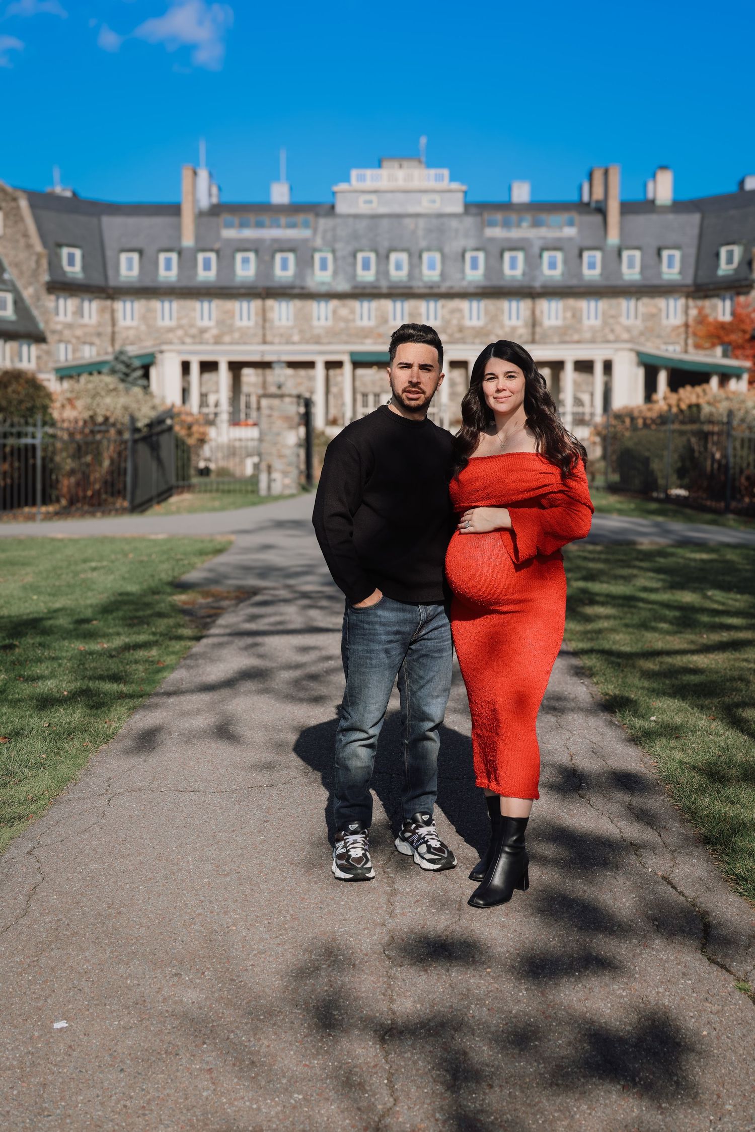 A couple poses together in front of a grand historic building on a sunny day.
