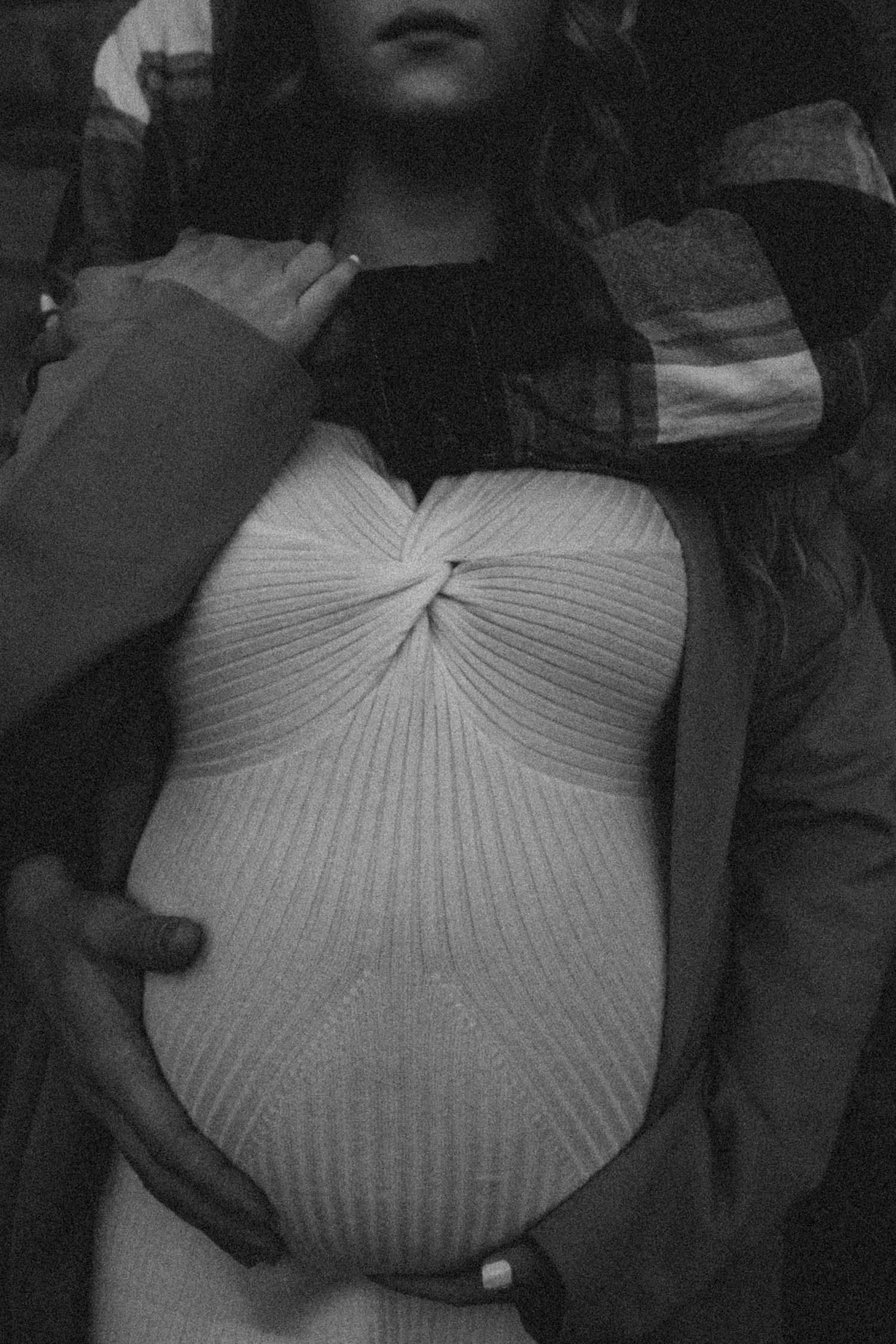 A black and white photo of a person wearing a ribbed white bodysuit and dark jacket.