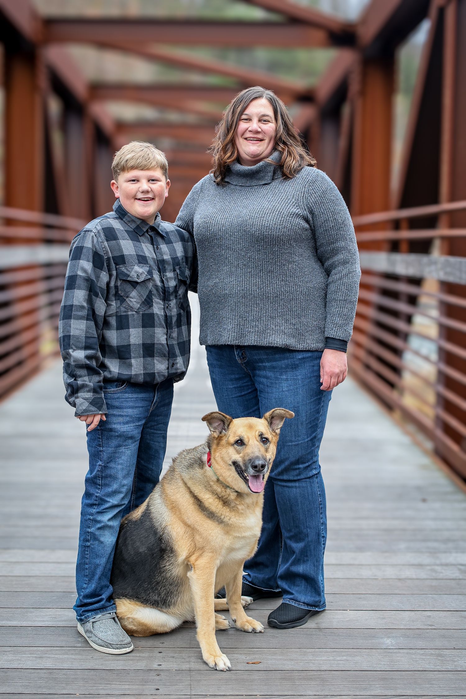 A German Shepherd mix dog sits with family members on a wooden bridge during an outdoor photo session.