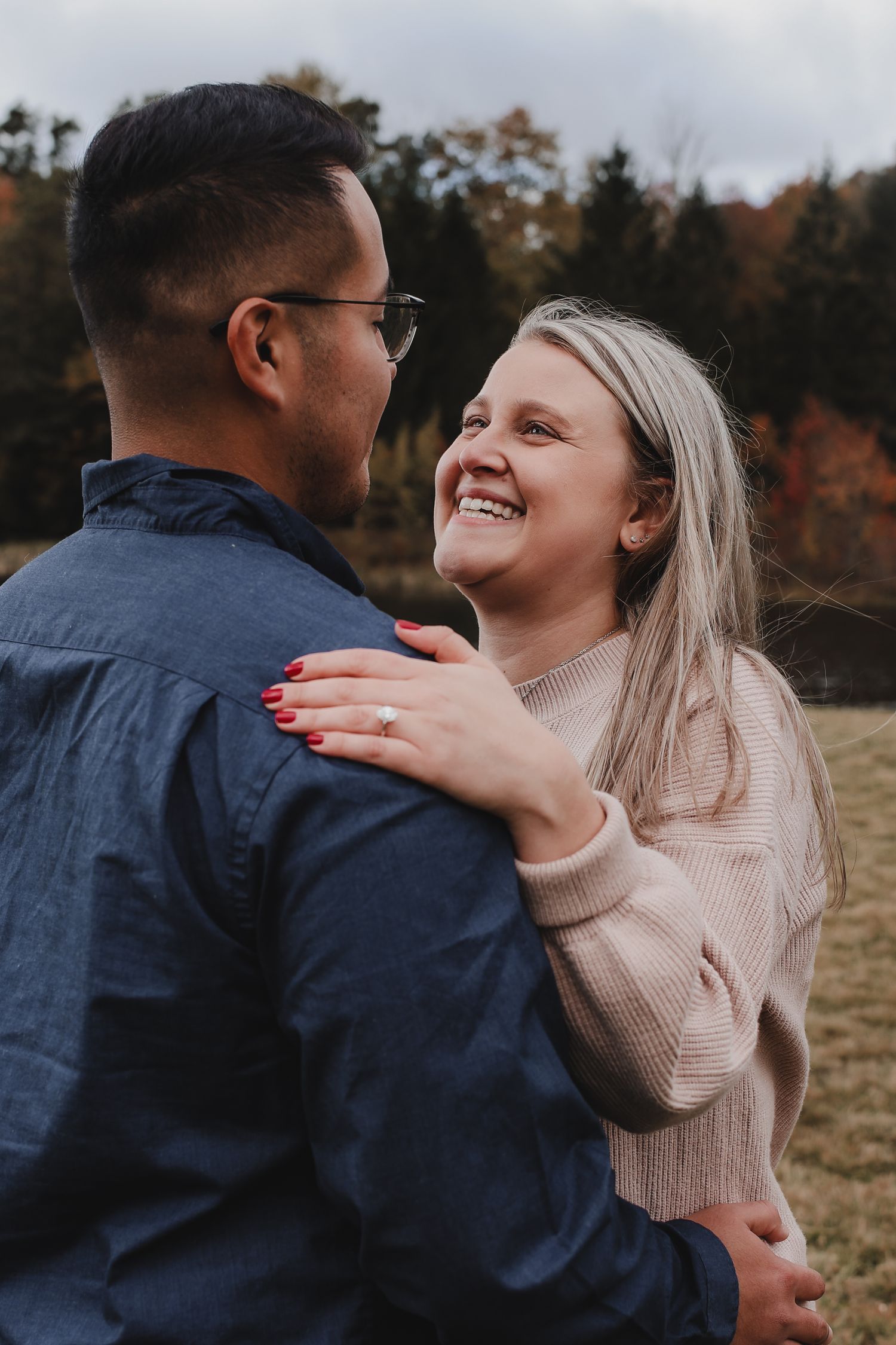 A couple shares a joyful moment together outdoors during autumn, embracing and laughing in casual sweaters.