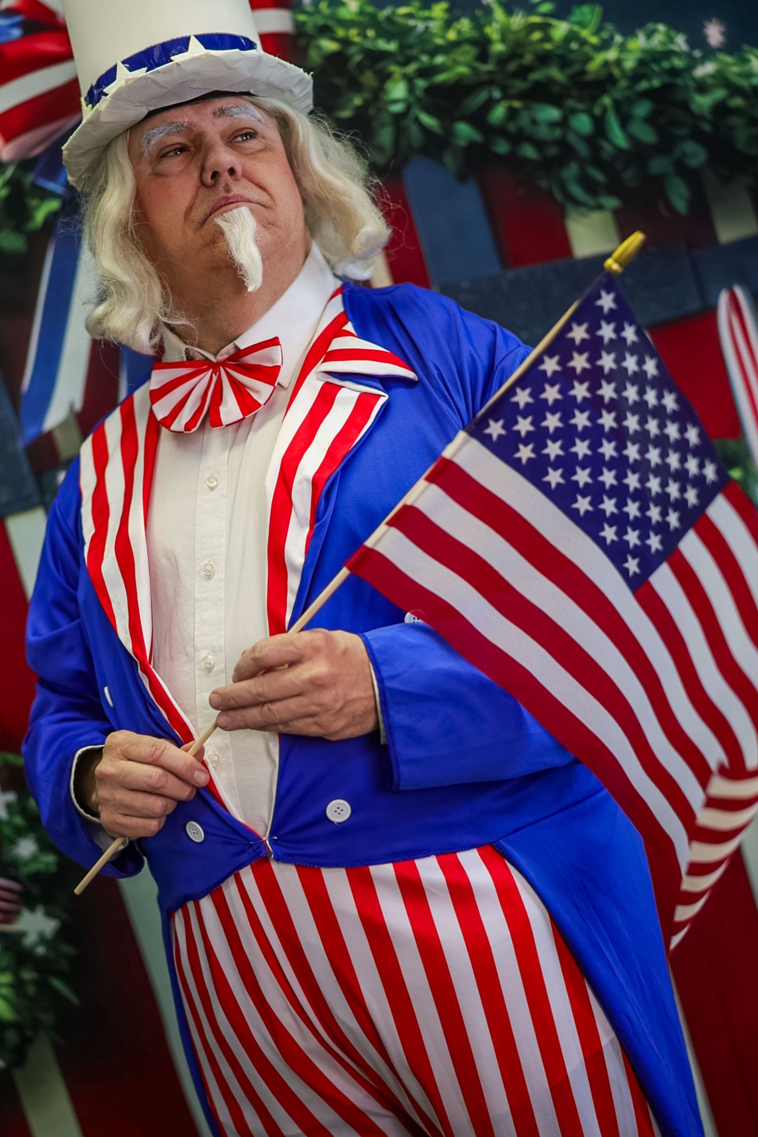 Man dressed as Uncle Sam in patriotic red, white, and blue costume holding American flags at a Fourth of July celebration.
