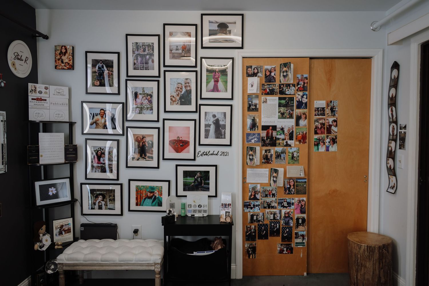 A gallery wall of black and white photographs and framed artwork hangs in a white hallway space.