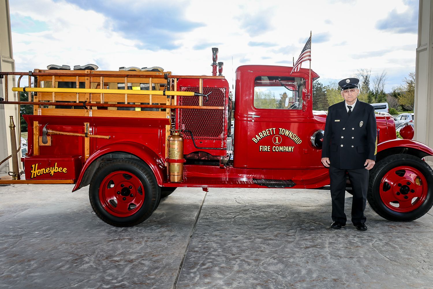 Vintage red Barrett Township Fire Company truck named Honeybee parked outside station with firefighter in uniform.