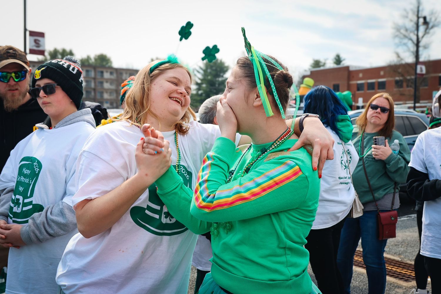 Two women in green St. Patrick's Day outfits laugh and embrace outdoors at a festive celebration.