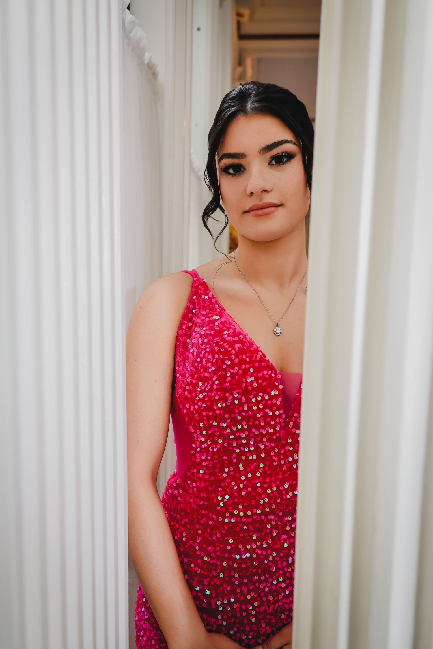 Young woman in a sparkling pink sequin dress posing elegantly between white columns for a formal event.