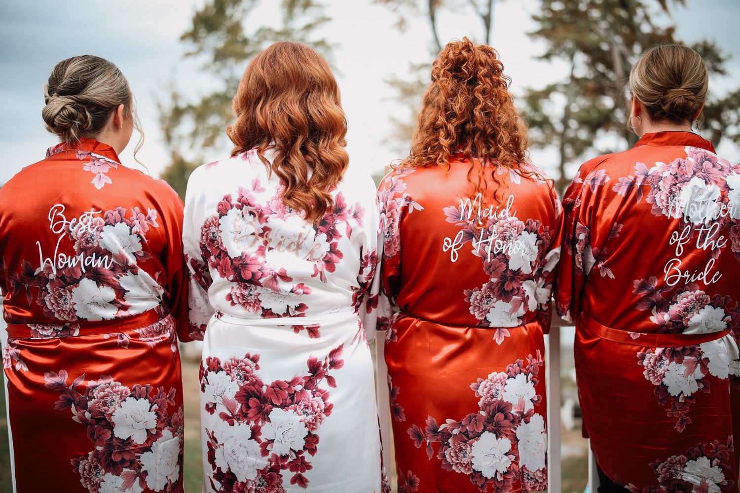 Four people wearing floral red and white silk robes stand together showing their backs to the camera.