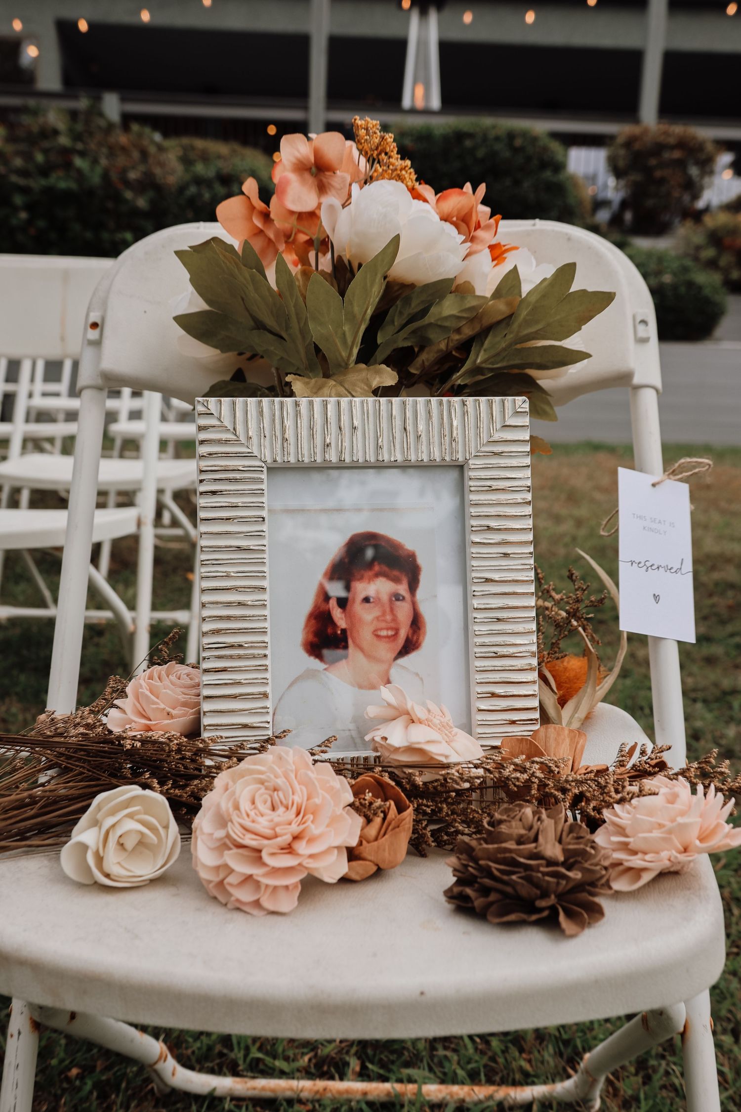 Vintage framed photographs displayed on white chairs with blush and brown floral decorations at a wedding memorial table.