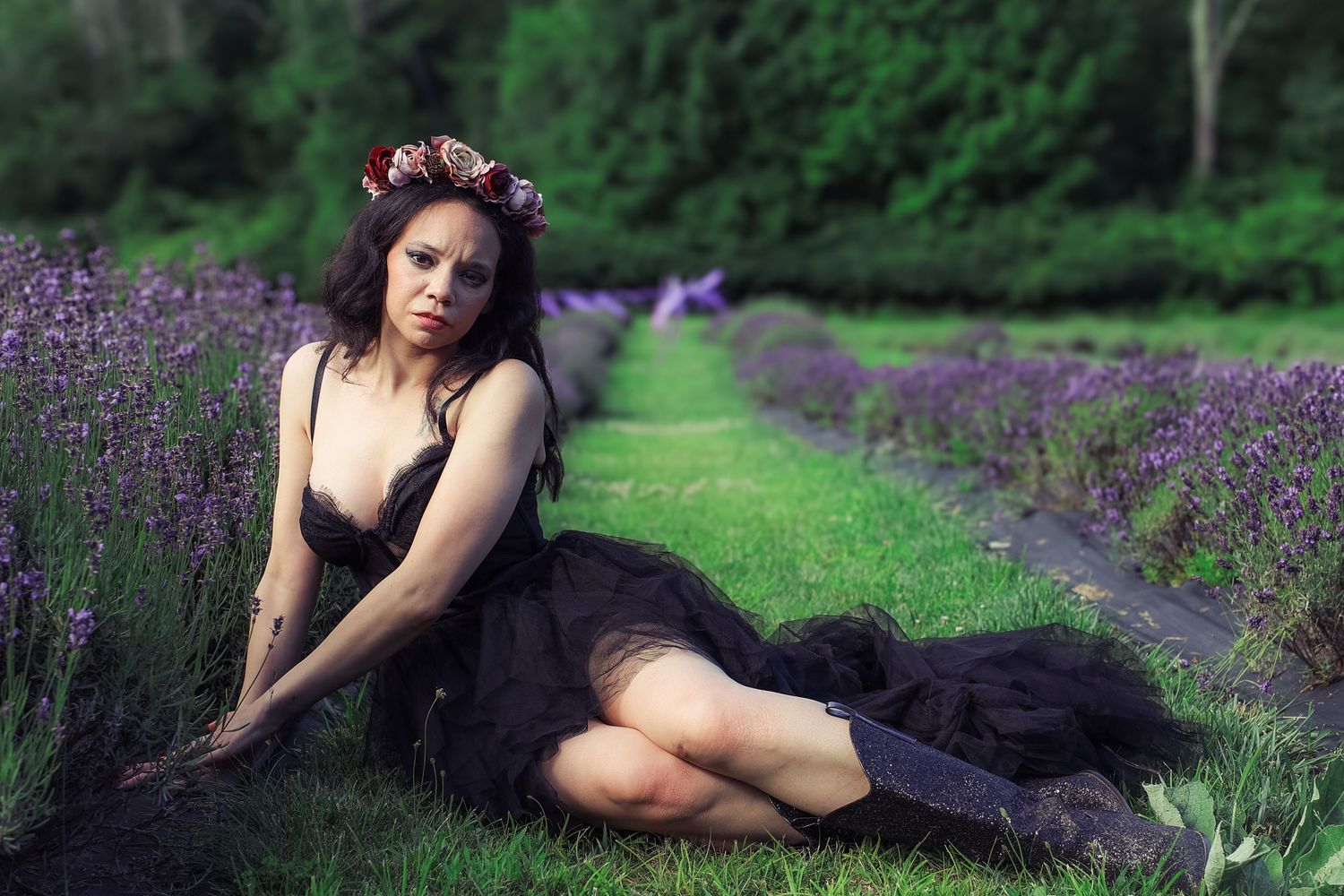 A figure in a black dress poses gracefully among blooming purple lavender flowers in a garden setting.