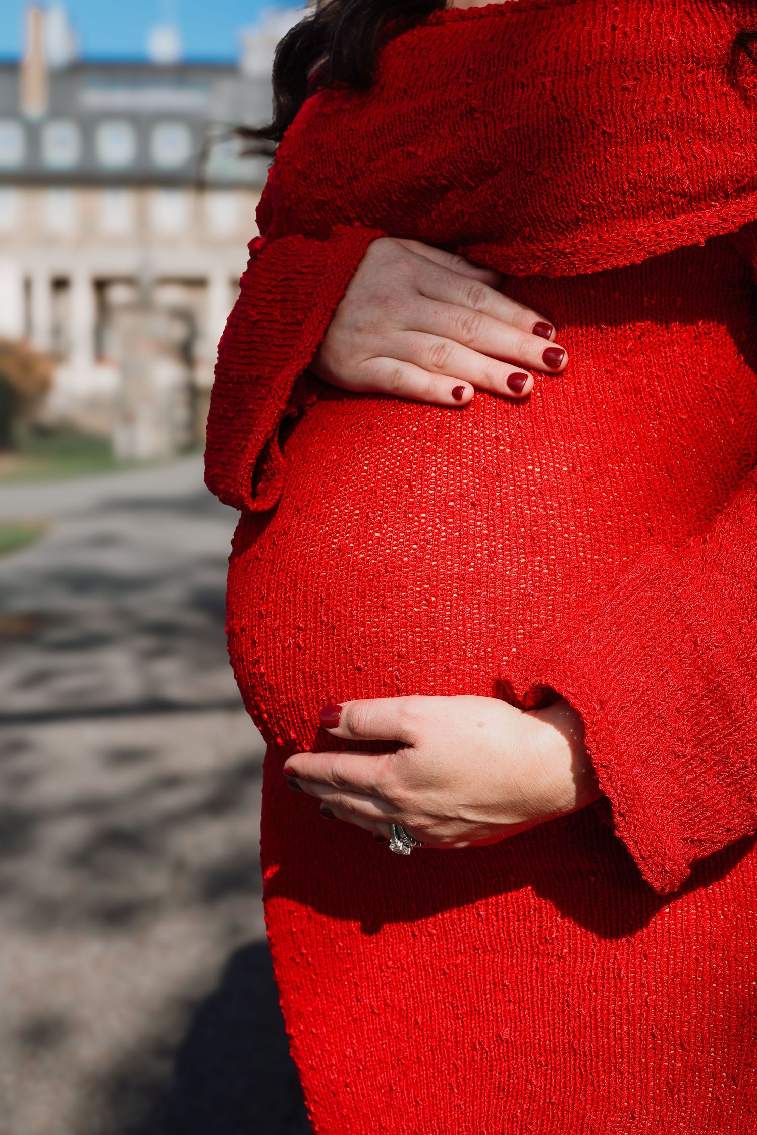 Close-up shots of hands cradling a pregnant belly covered in a bright red knit sweater against a blurred background.
