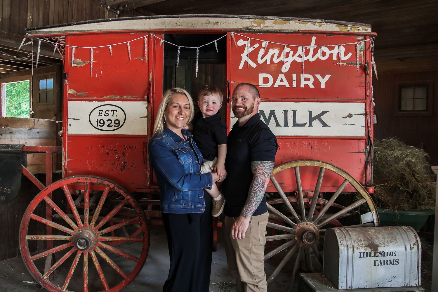 Vintage red milk delivery wagon with wooden wheels and Kingston Dairy signage displayed outside a rustic building.