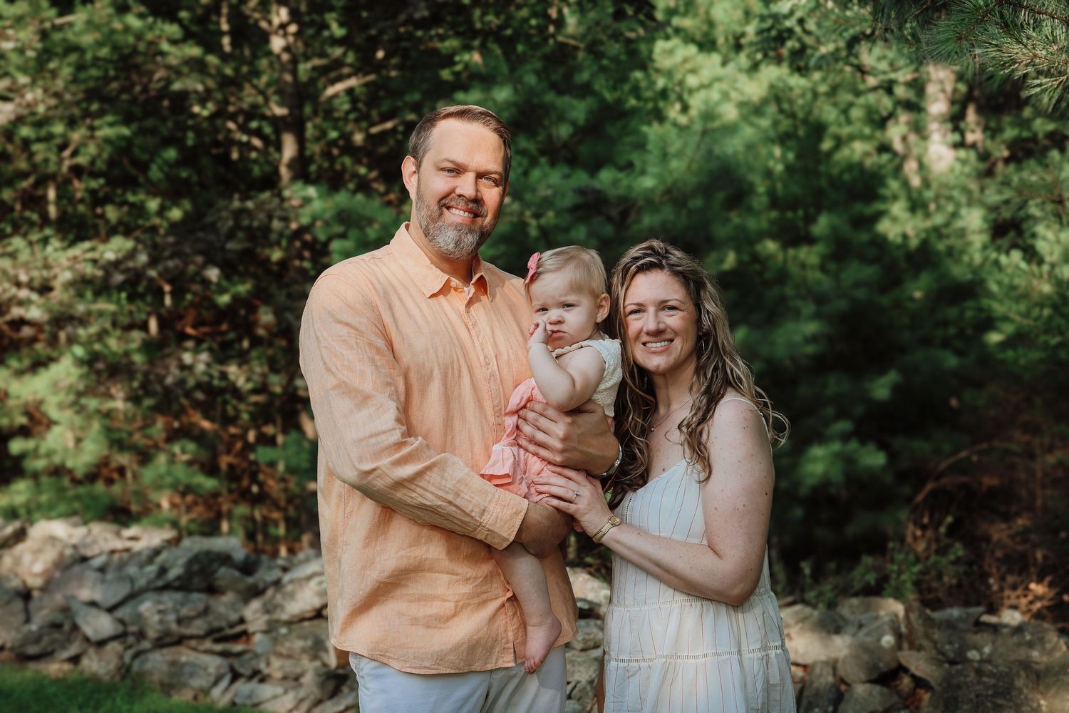 A couple in coordinating peach and white outfits shares romantic moments in a lush green forest setting.