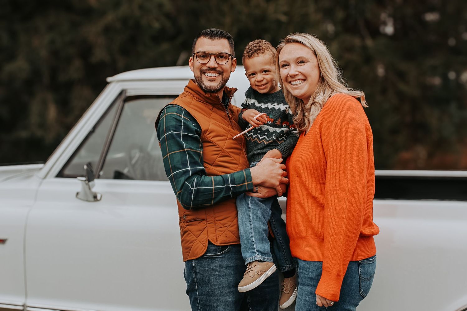 Family wearing coordinated orange and green outfits poses together in front of a white vintage car.