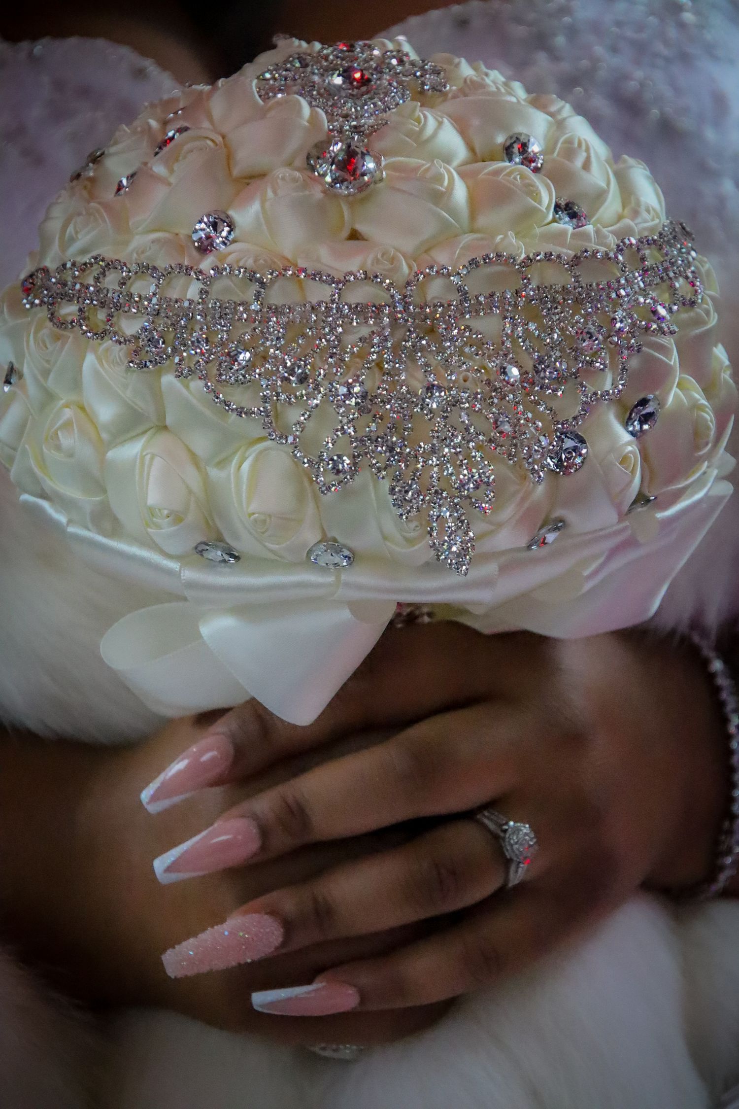 Close-up view of elegant bridal bouquet with crystal embellishments and pink manicured nails holding white roses.