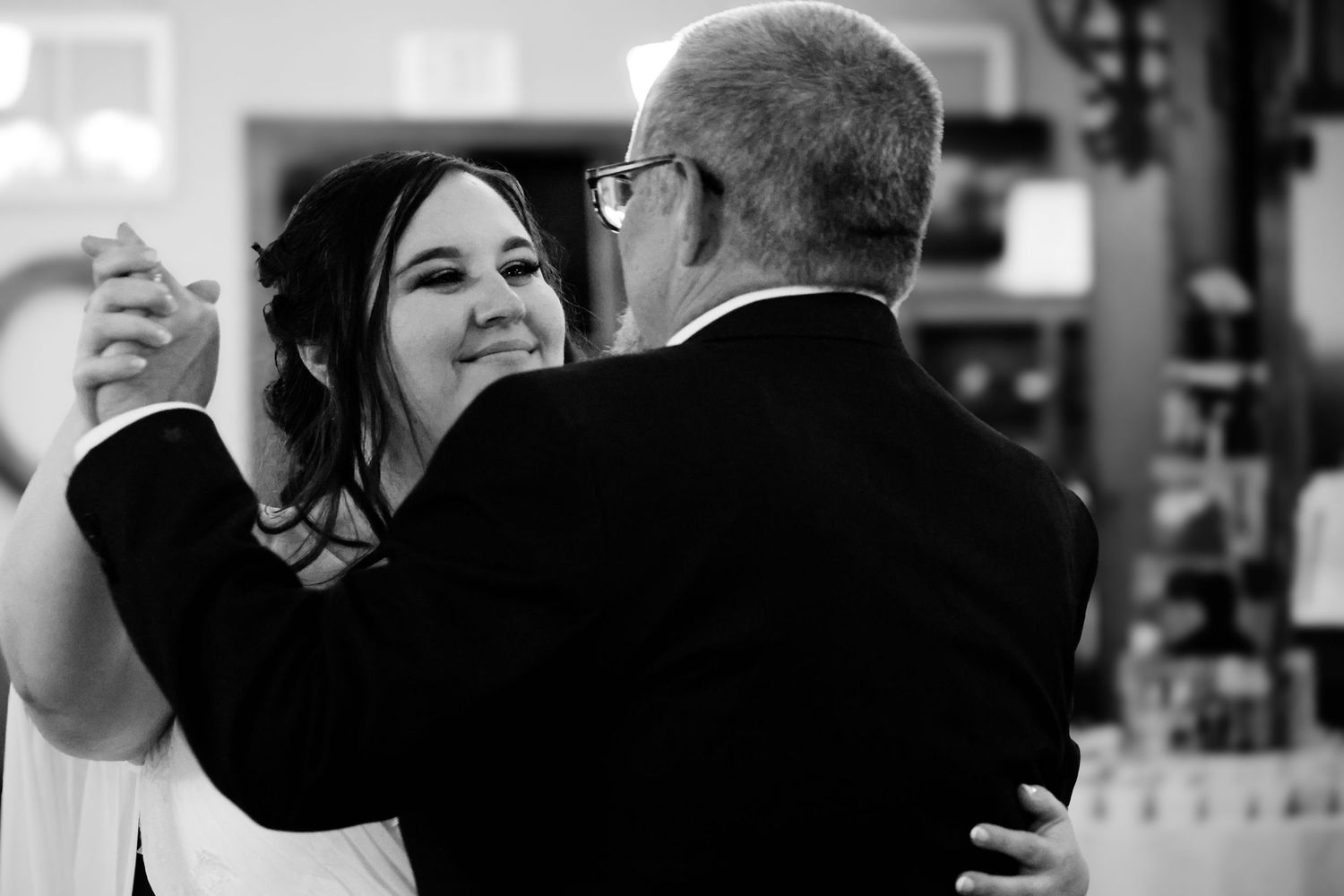 A tender black and white moment captured during a father-daughter dance at a wedding reception.