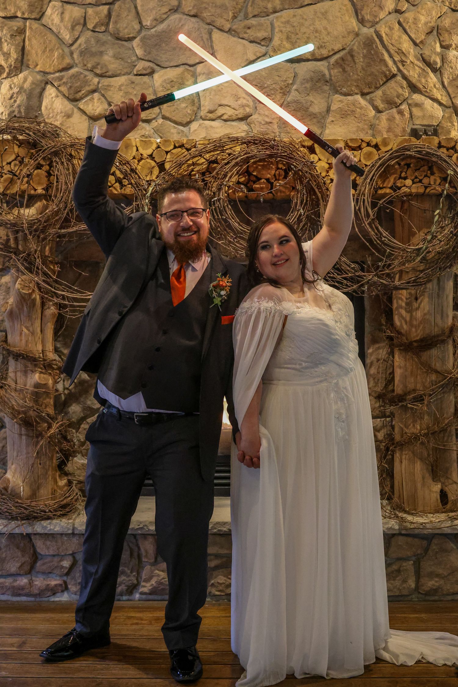 A wedding couple poses playfully with lightsabers in a stone-walled venue during their celebration.