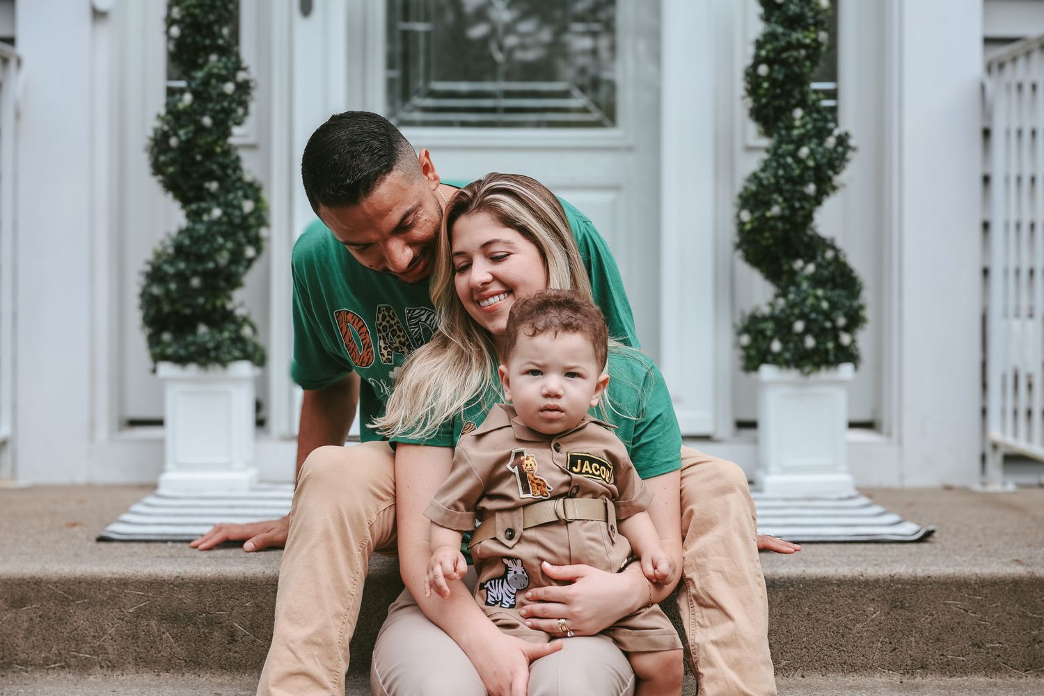 Family shares a joyful moment together while sitting on front porch steps with decorative greenery in background.
