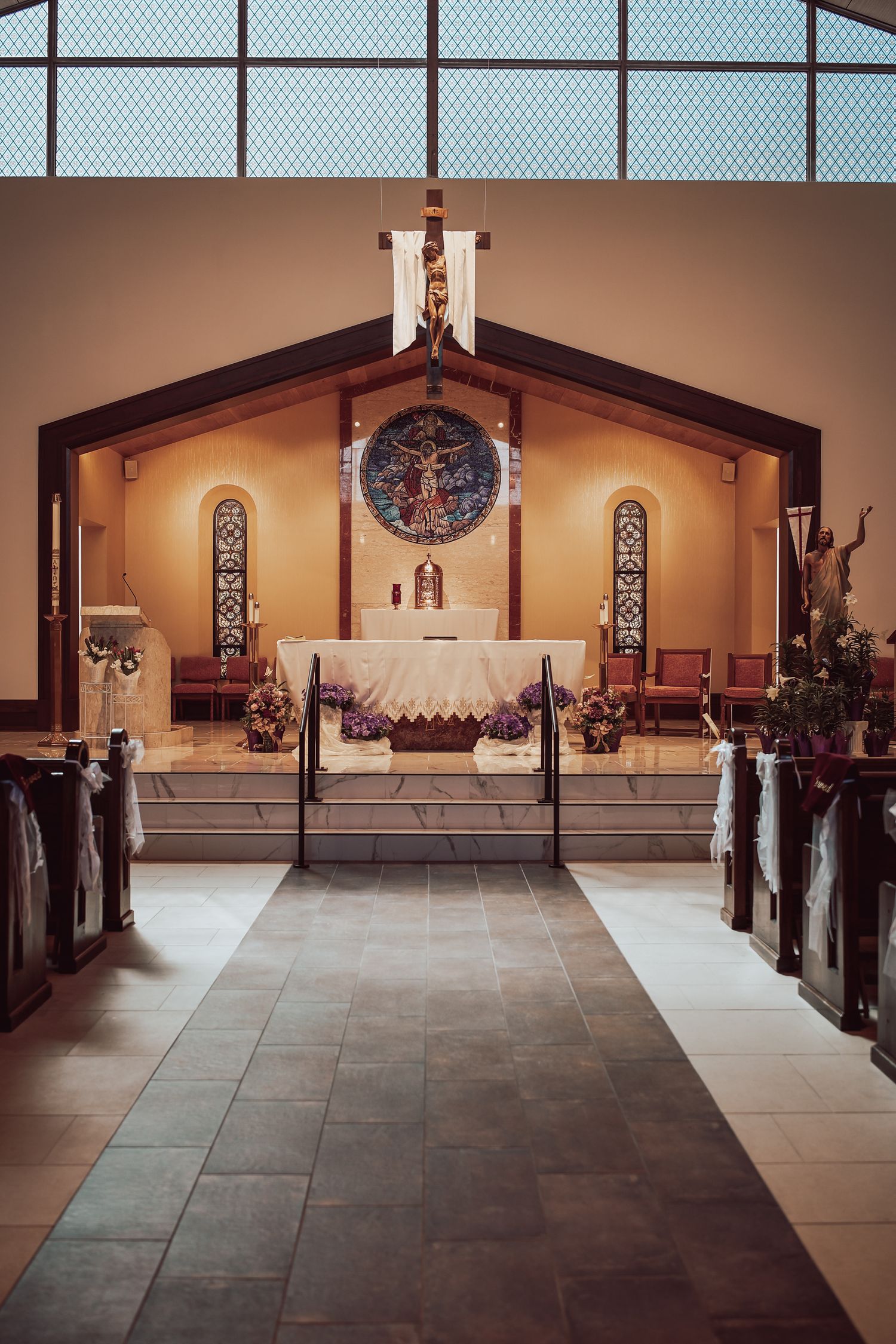 Interior panorama of a modern church sanctuary with wooden pews and stone flooring under warm lighting.
