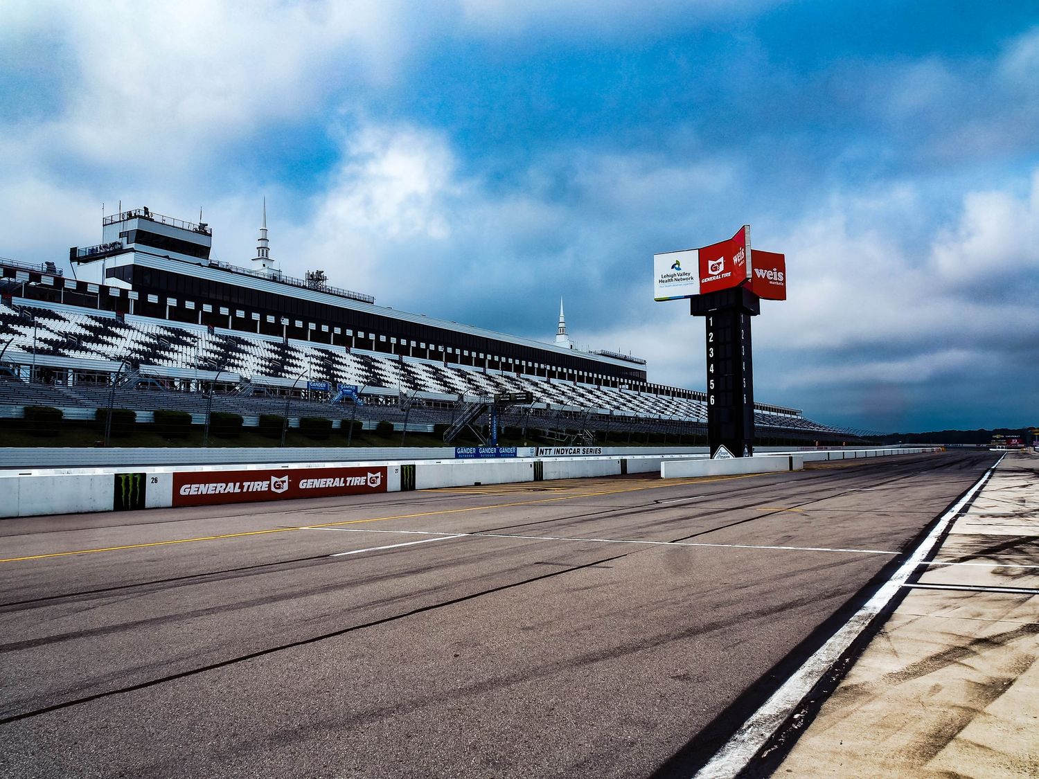 Race track at Pocono Raceway showing multiple angles of the banked turns and grandstands under cloudy skies.