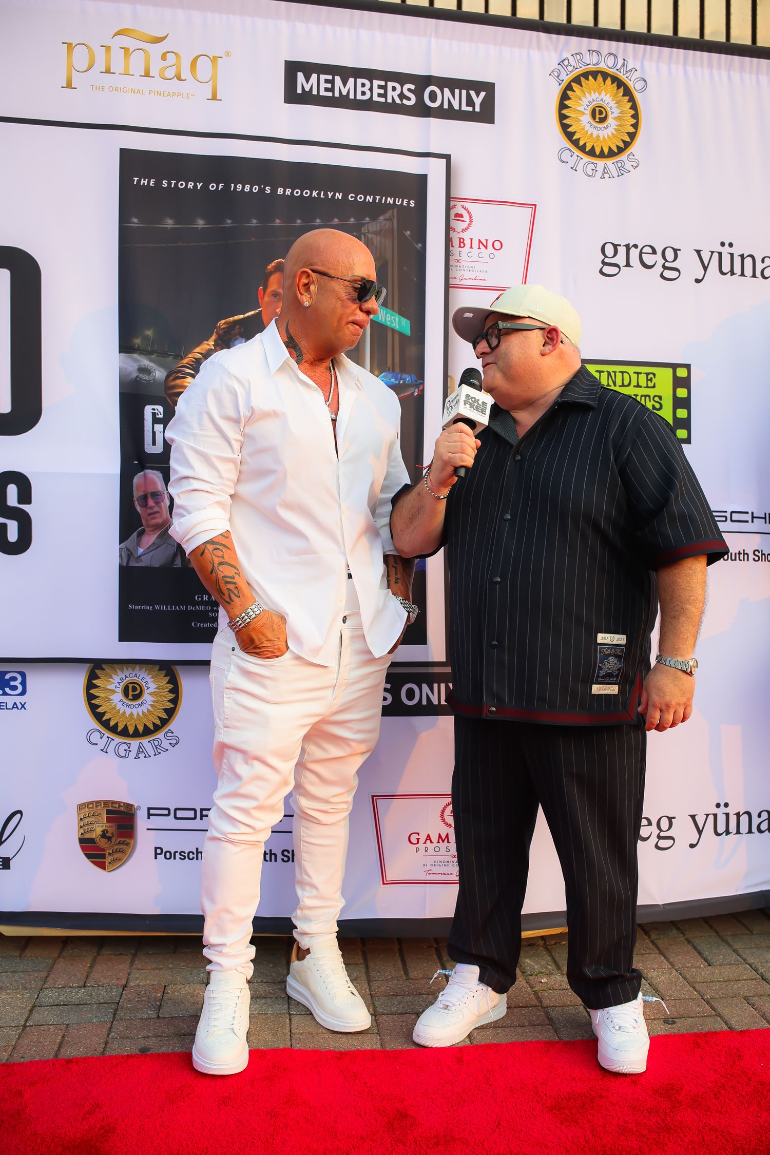 Two people in contrasting black and white outfits stand together on a red carpet at an event with posters on the wall.