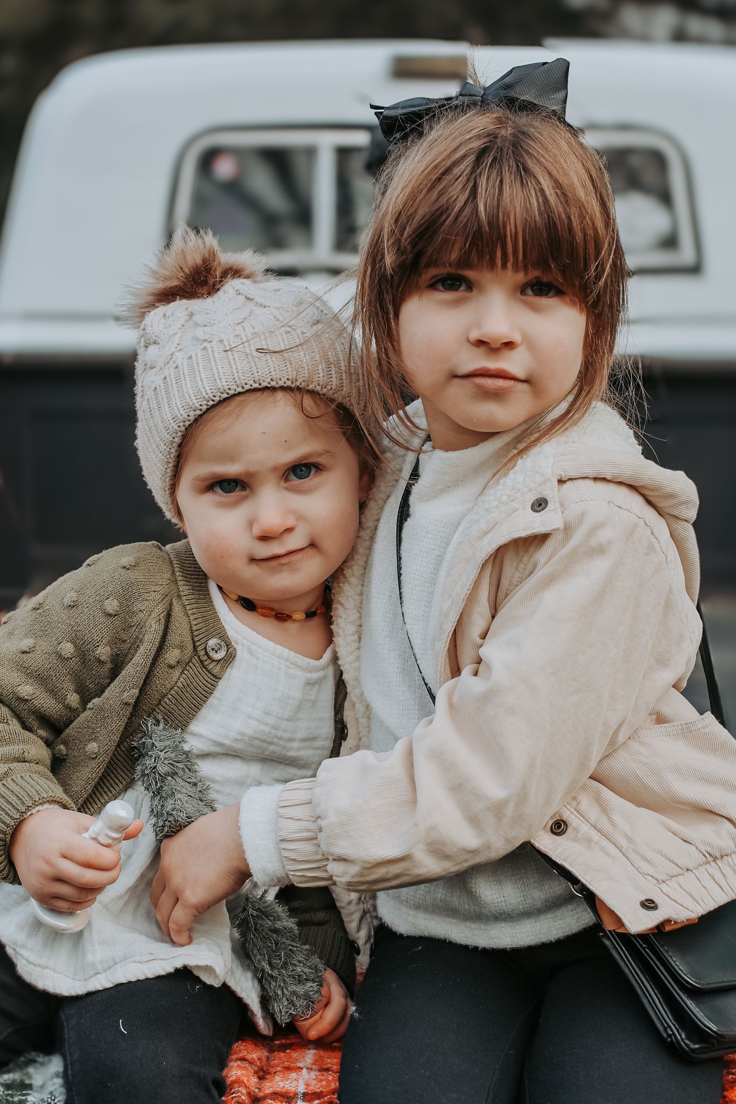 Two young children in cozy winter outerwear sit close together in a series of candid outdoor portraits.