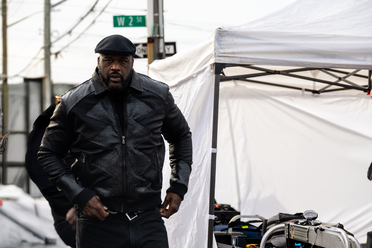 Someone wearing a black winter coat and beanie stands near a white tent on a street corner.