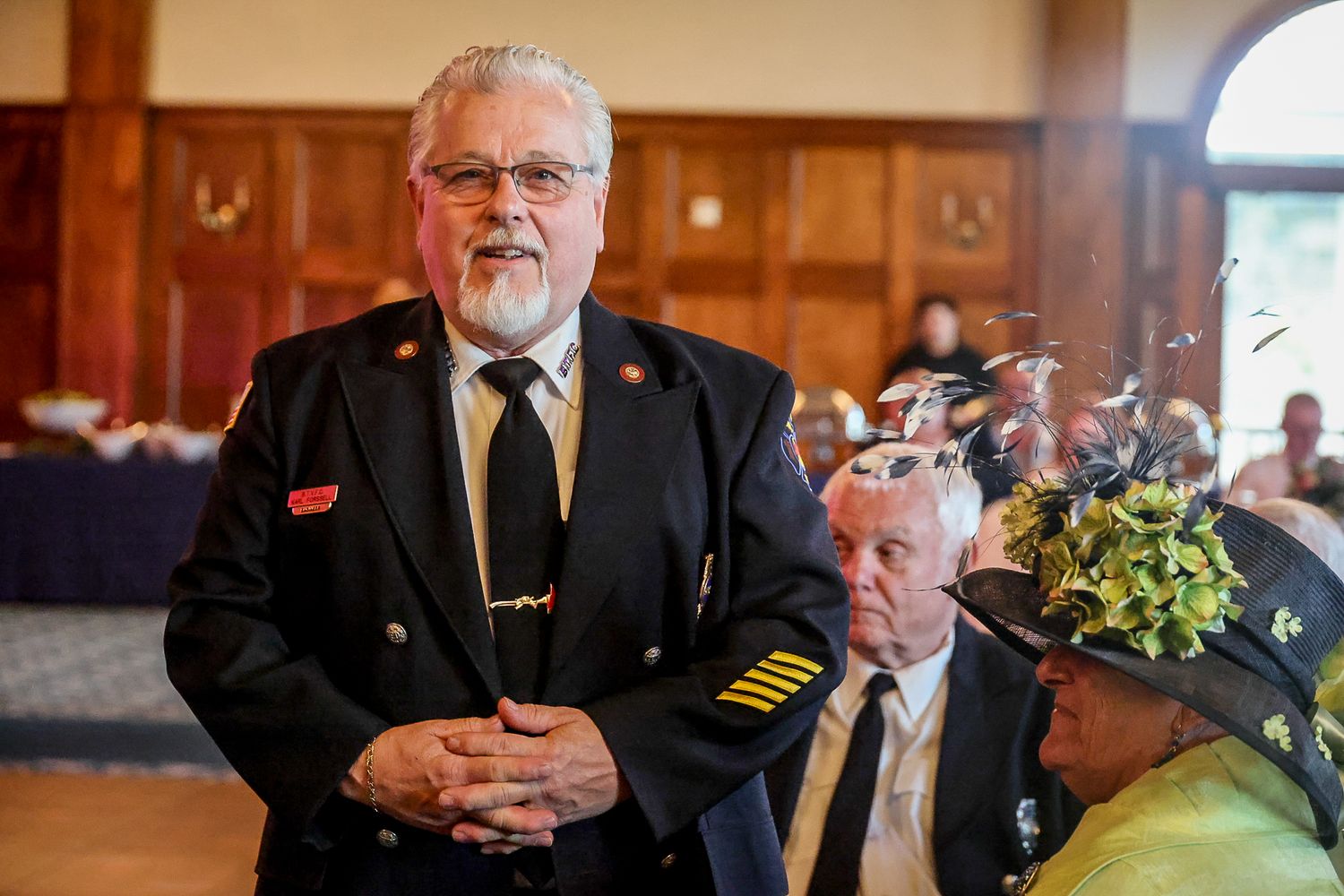 Man in military dress uniform with gold buttons and red poppy pin stands at formal indoor ceremony.