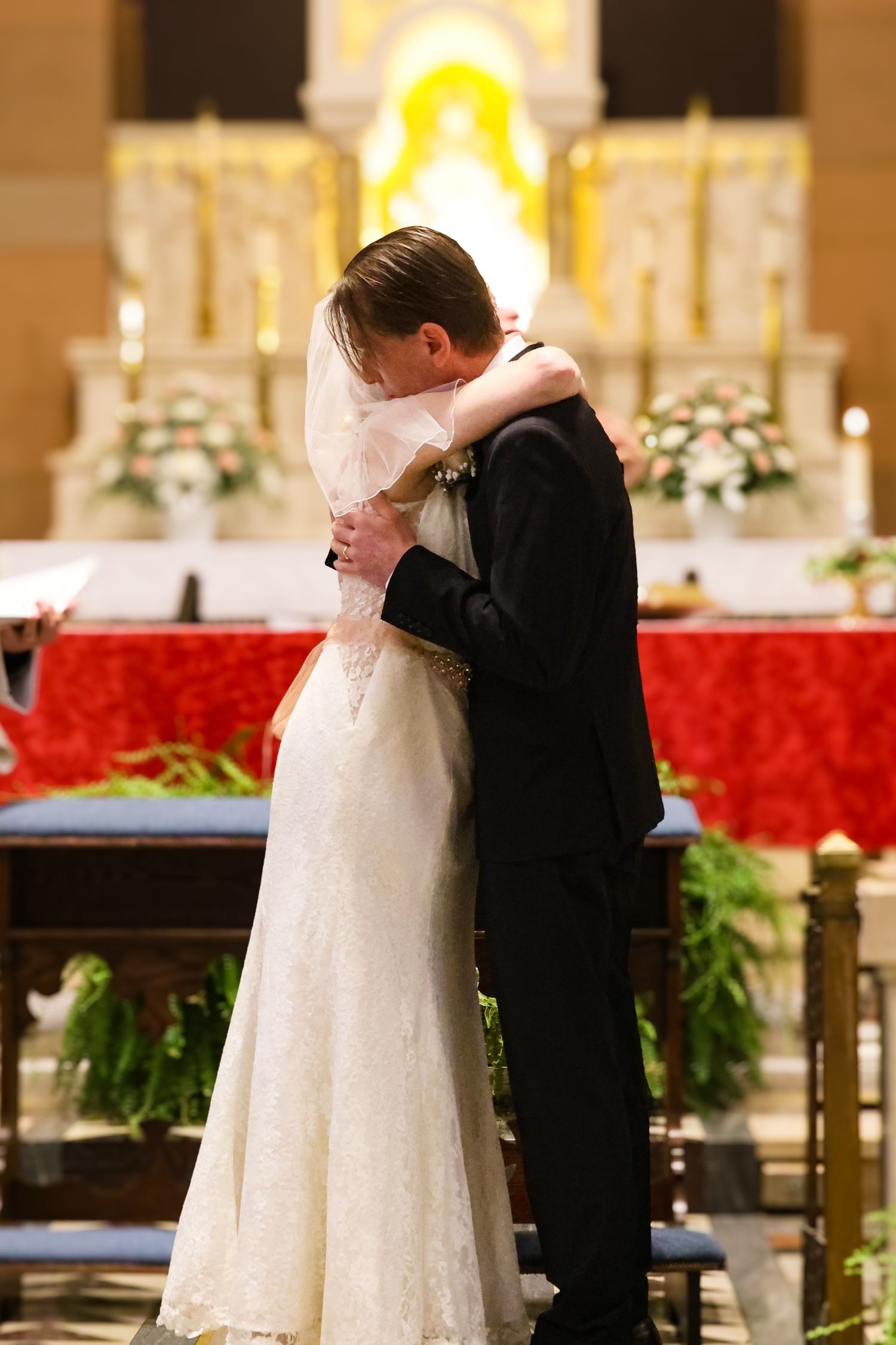 A couple shares their first kiss during a wedding ceremony in an ornate church with red poinsettias decorating the altar.