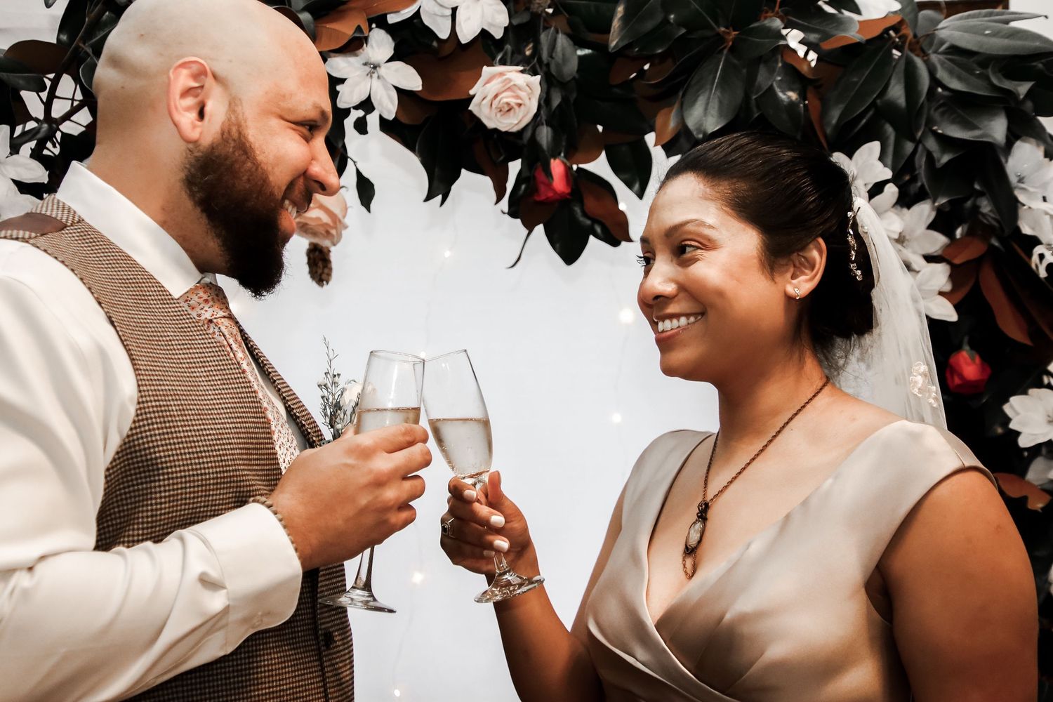 Two people share a celebratory toast with champagne glasses while smiling at each other during a wedding celebration.