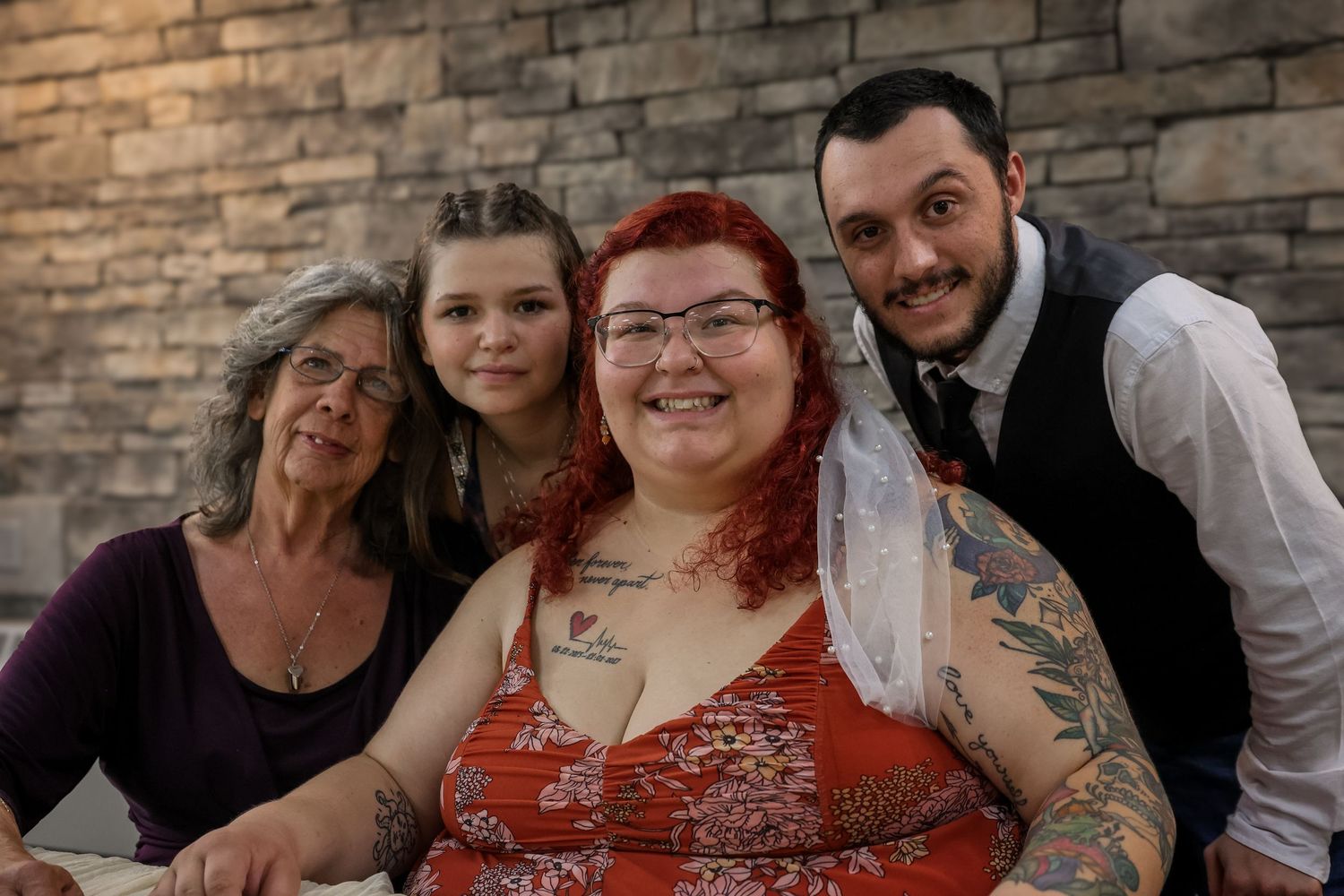 A group of four people posing together against a stone wall background.