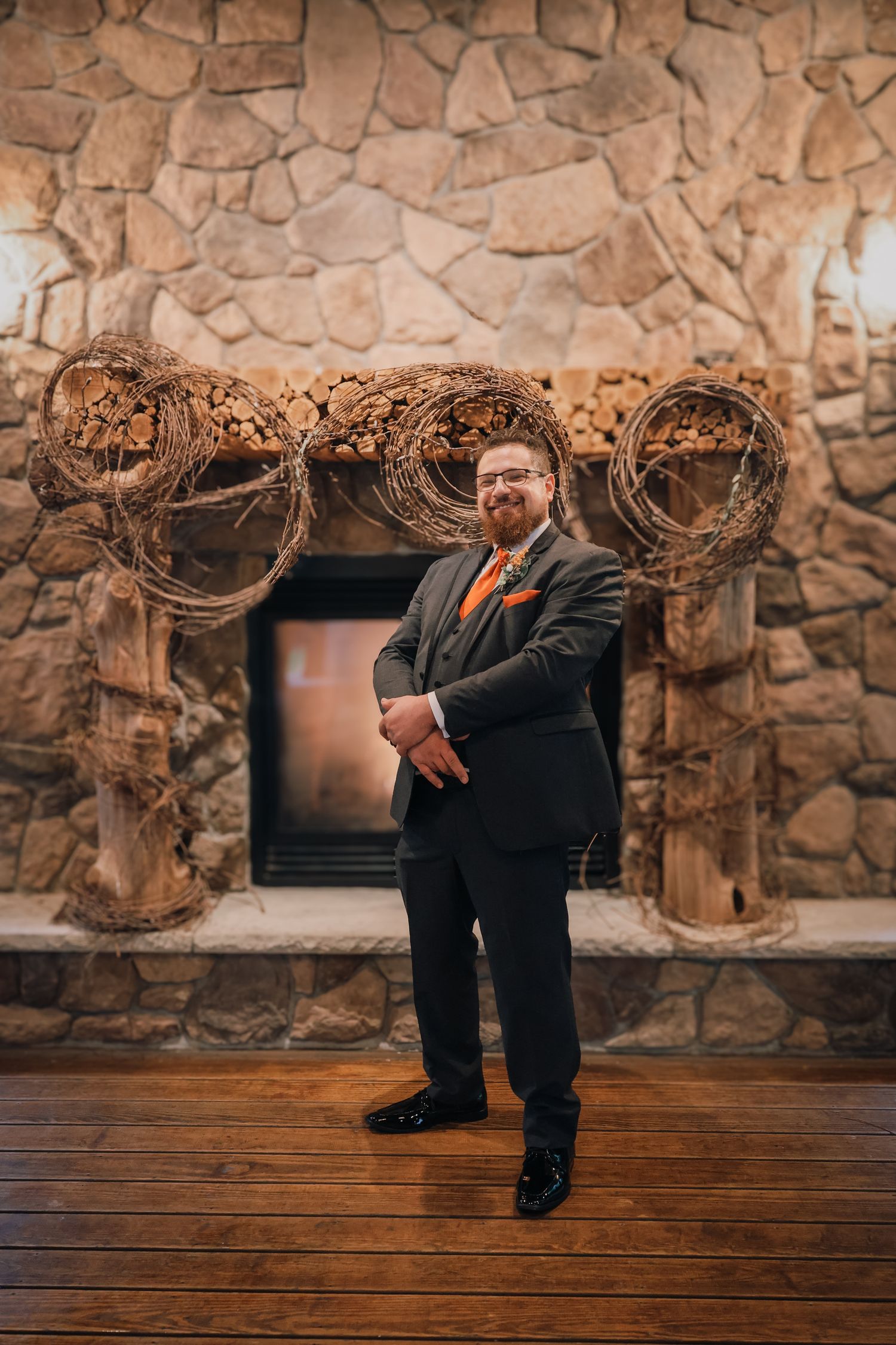 Person in a suit bends down to tie their shoe against rustic stone wall backdrop in wedding venue.