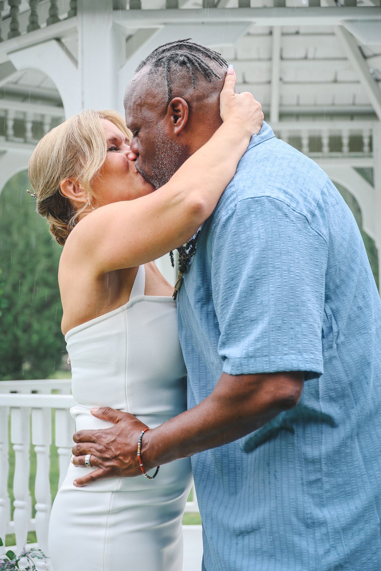 A romantic couple shares an intimate moment together outdoors in front of a white gazebo.