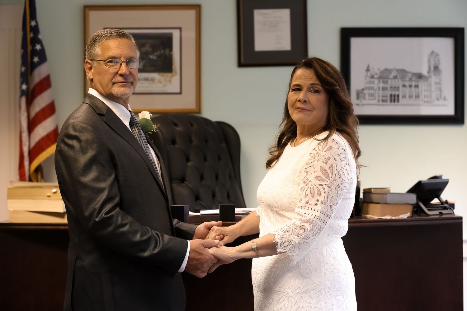 A formal ceremony takes place in an office with an American flag and framed artwork on the wall.