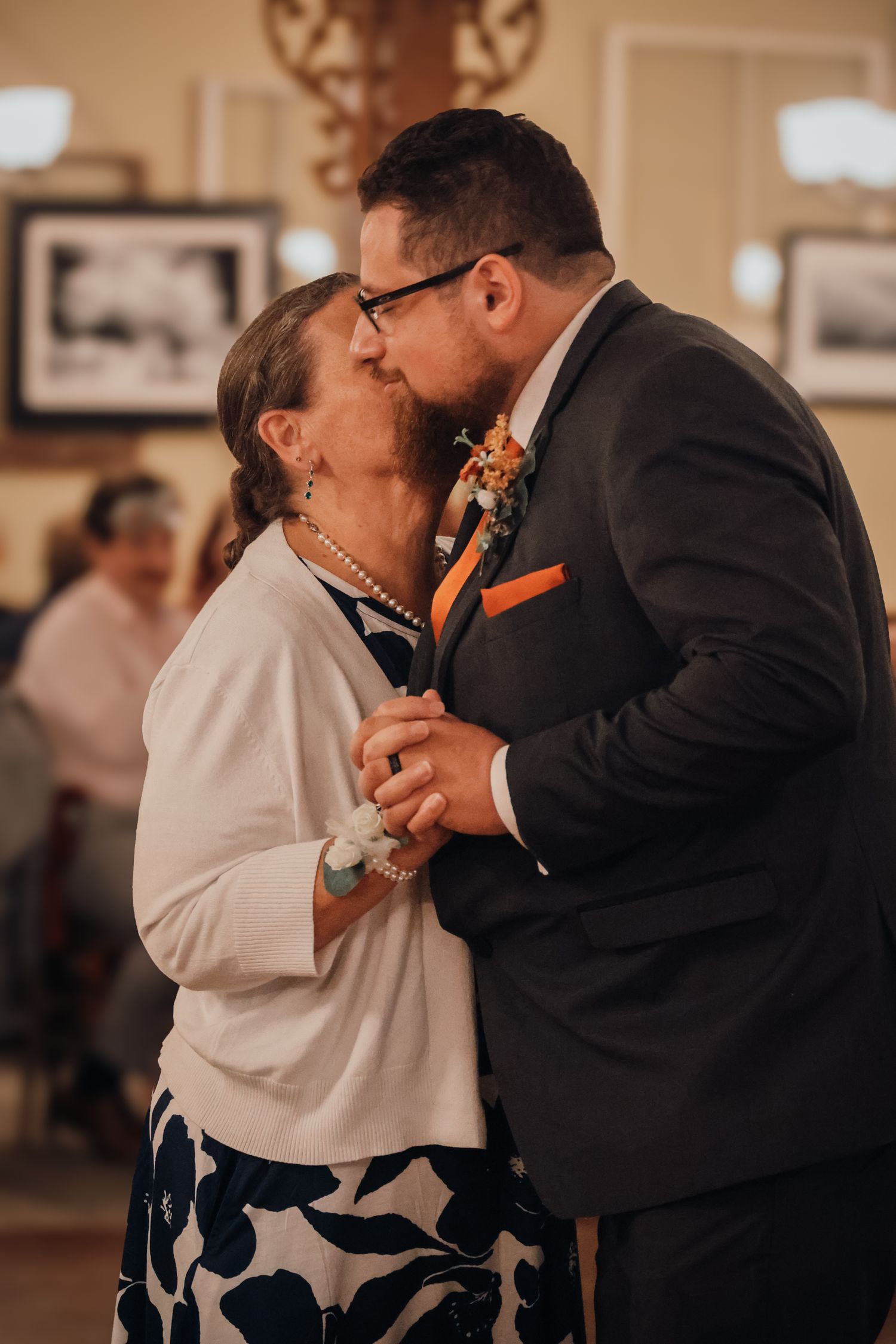 A couple in formal attire share an intimate dance moment in a dimly lit indoor venue.
