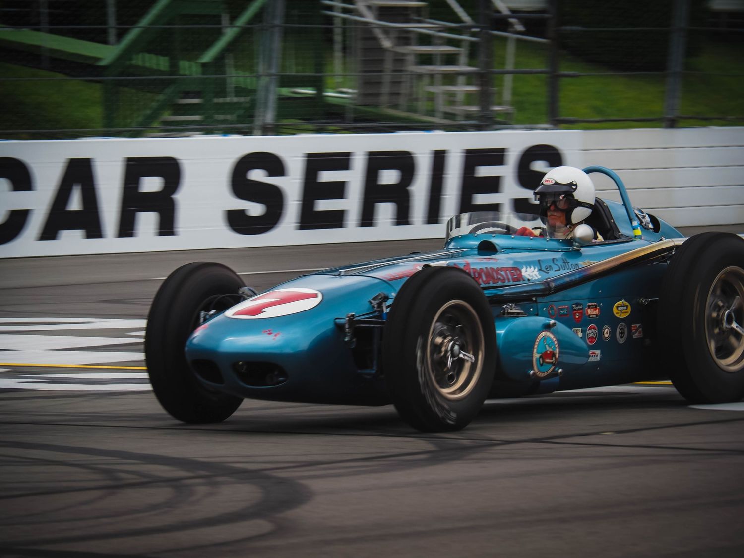 Vintage blue racing car speeds around track during classic motorsport competition.