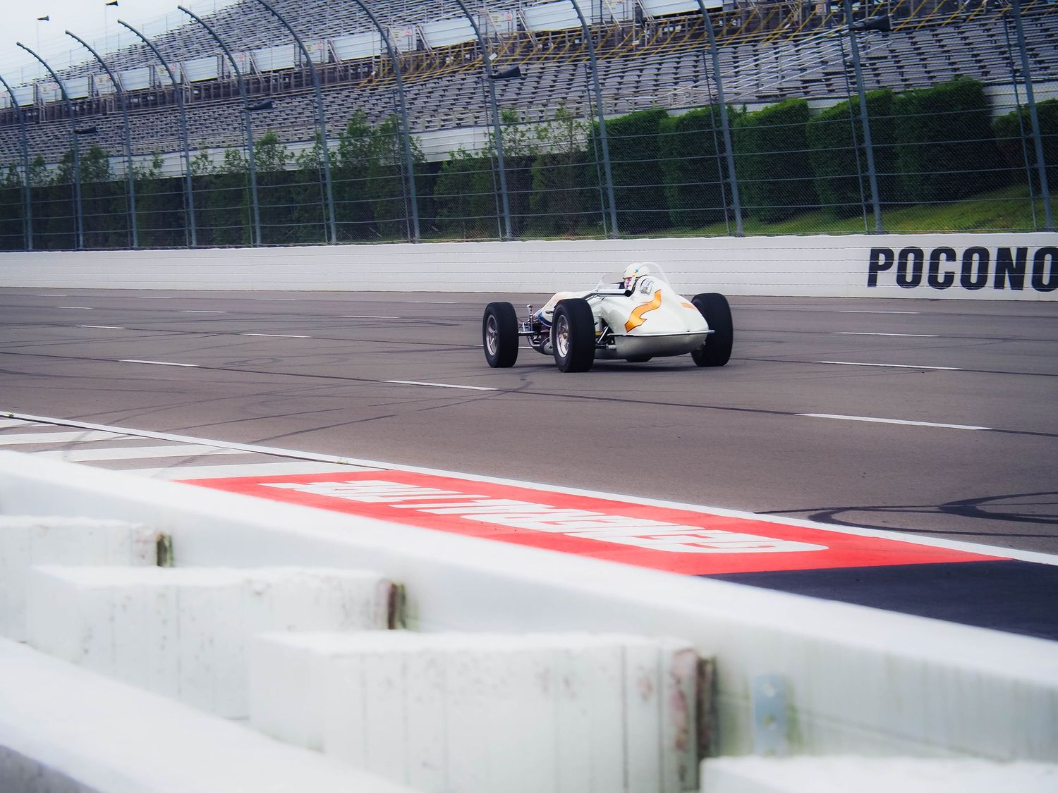 White race car speeds around the banked turn at Pocono Raceway during a motorsports competition.