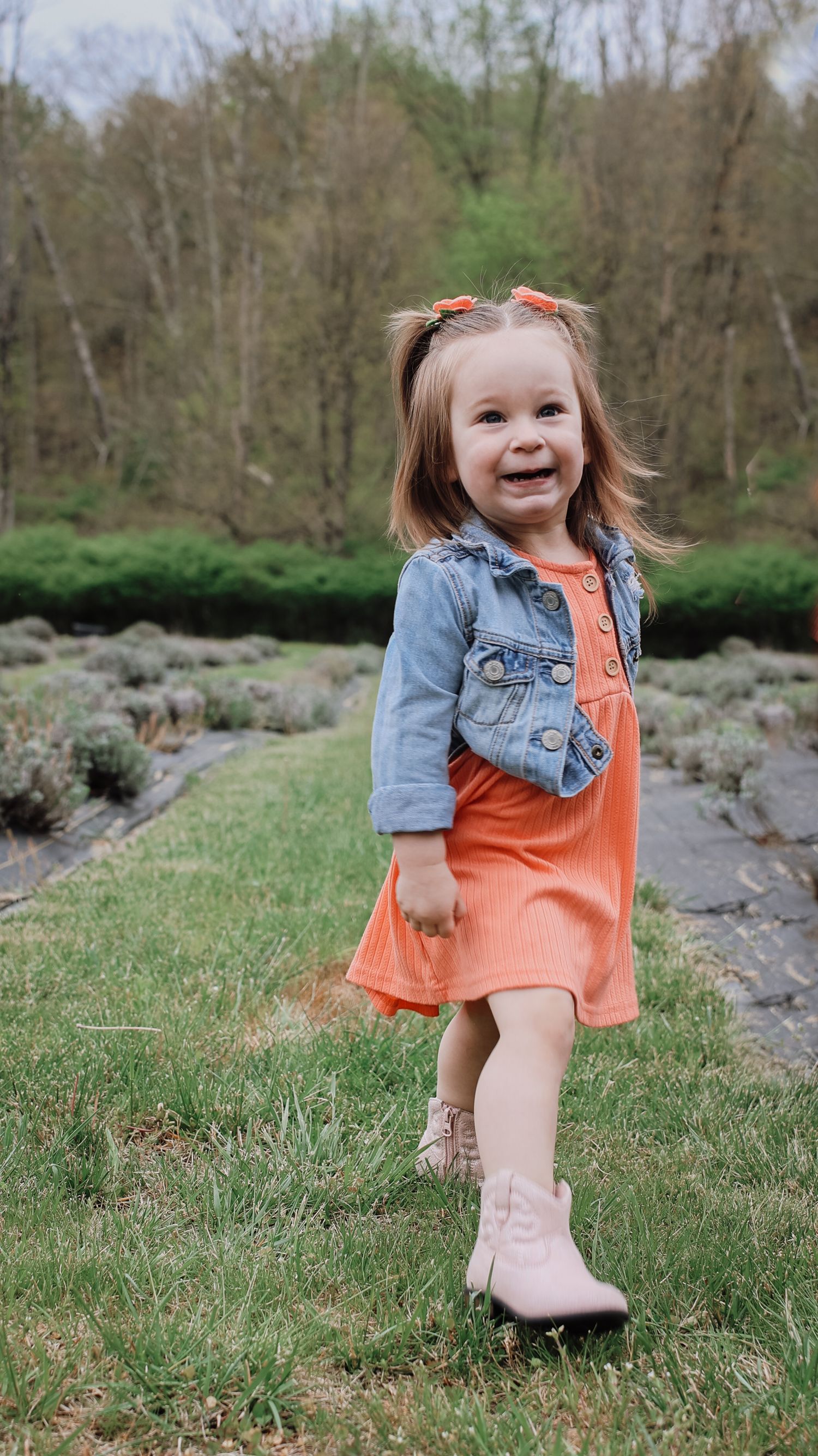 A series of outdoor photos showing a small child in an orange dress and denim jacket playing on grassy ground near rocks.