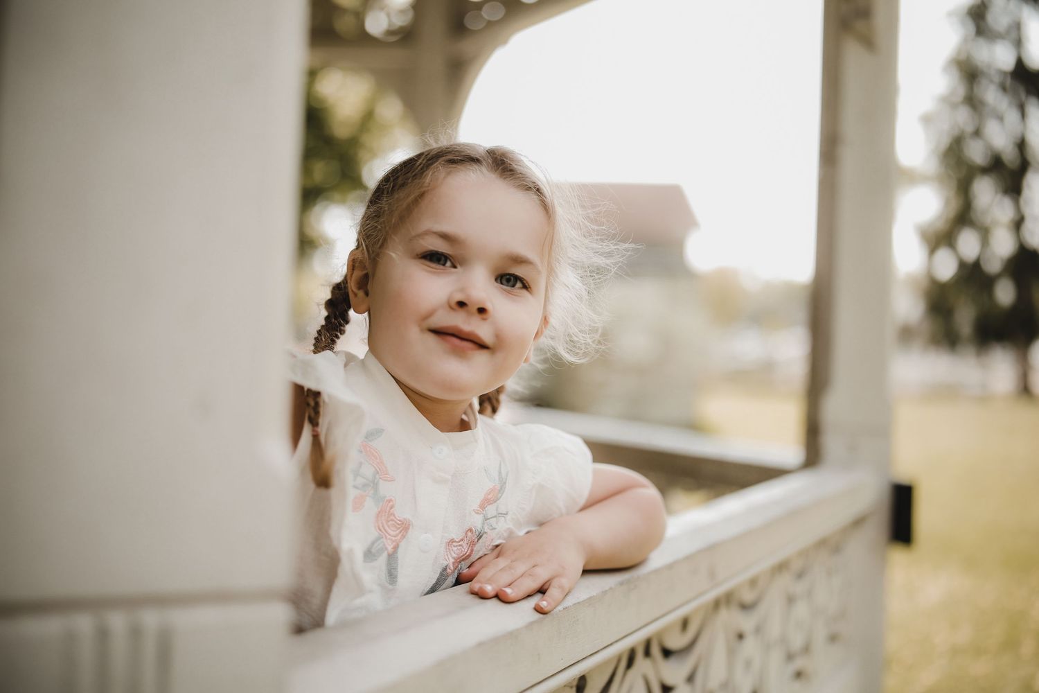 A child in a white dress sits on a porch swing during golden hour lighting.